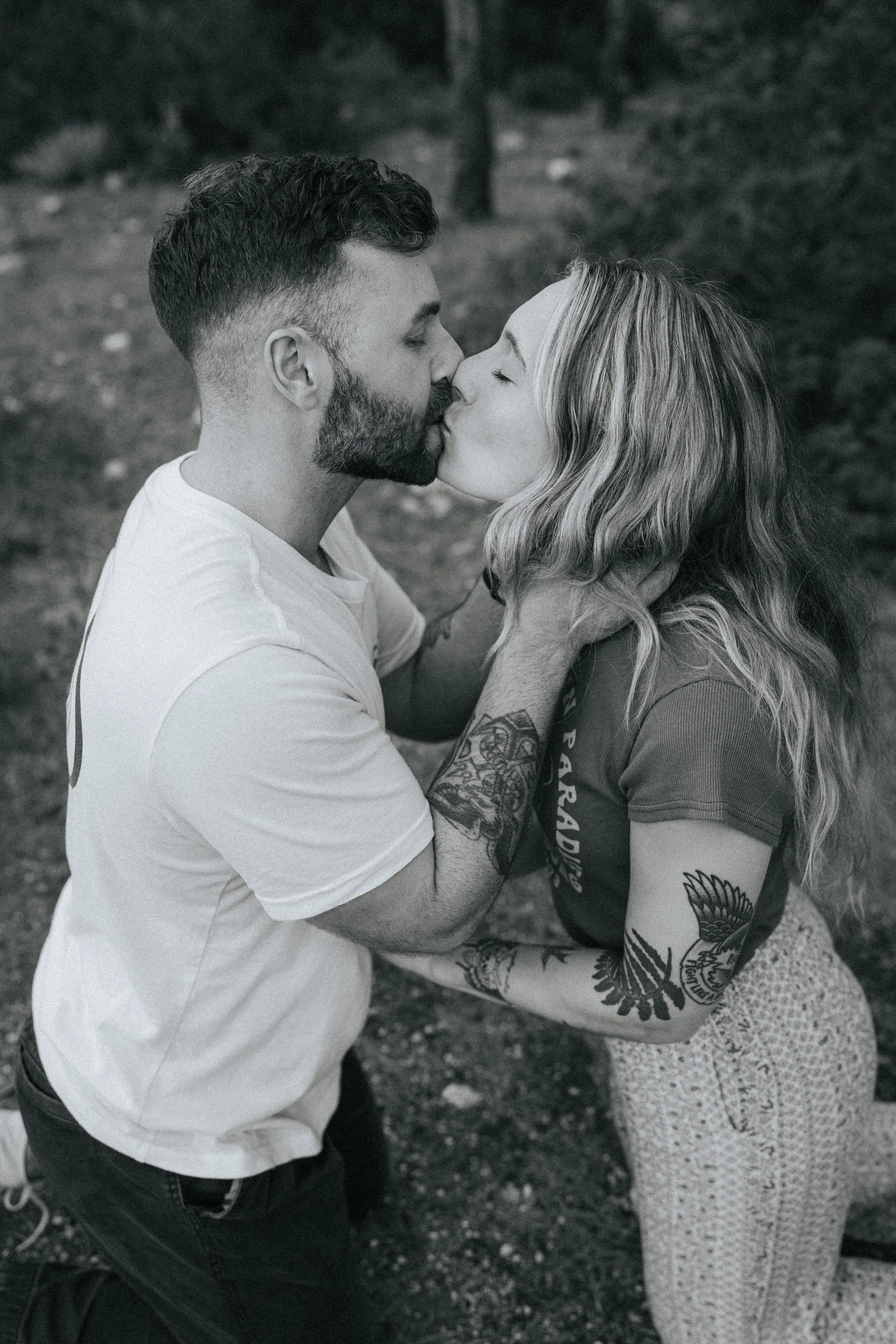 A black and white photo of a couple kissing and holding each other outside.
