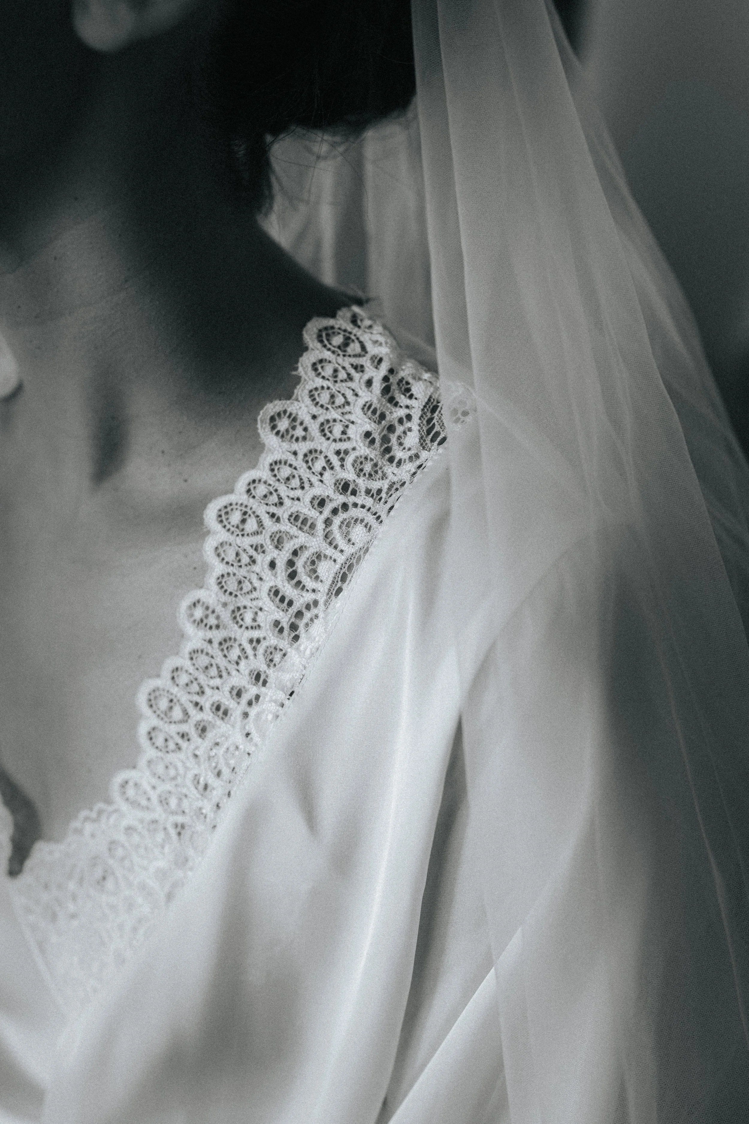 Close-up of a woman's shoulder and part of her face, wearing a white lace garment and a veil.