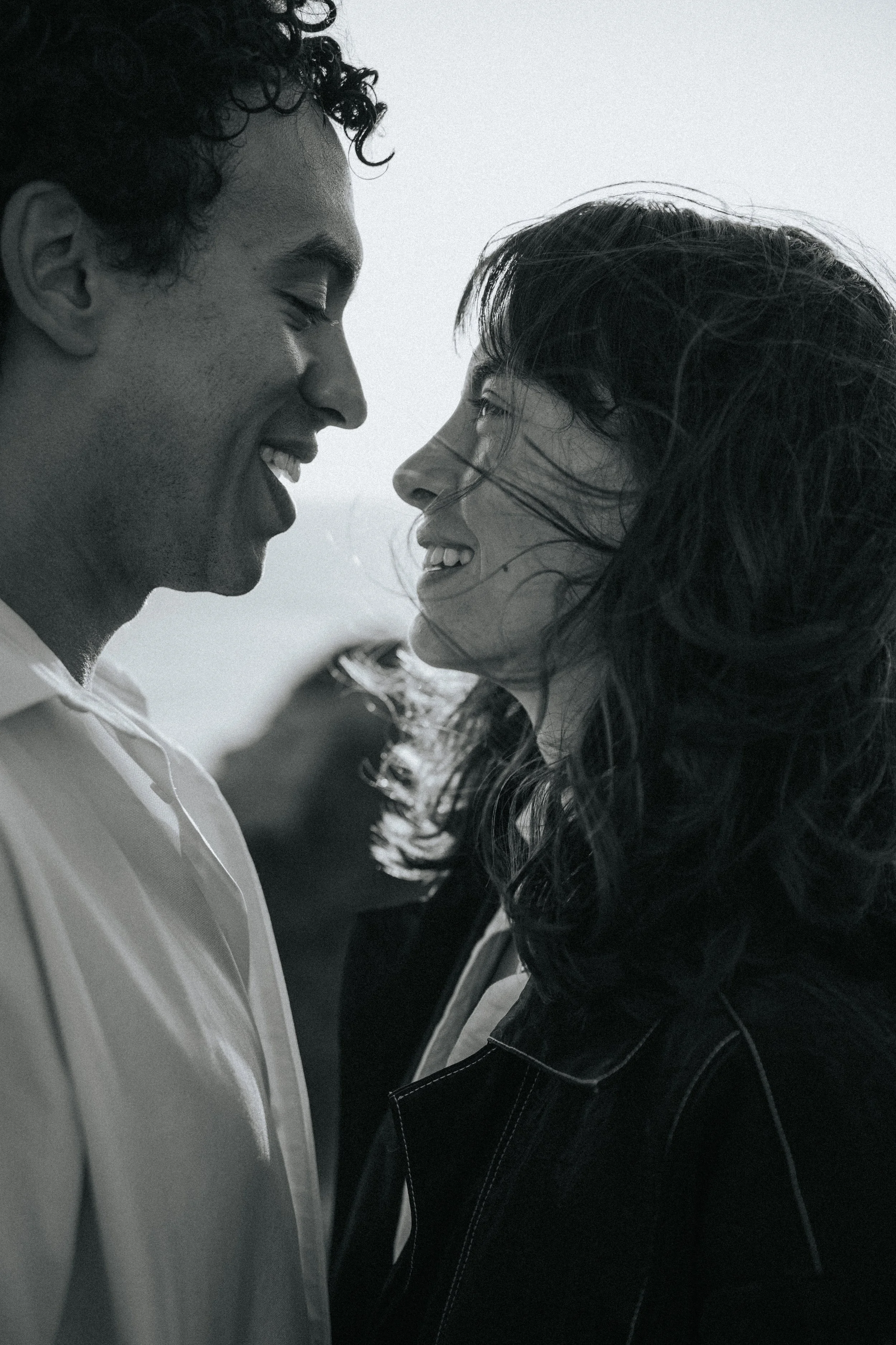 A black and white photo of a young man and woman close together, smiling and leaning their foreheads against each other, with their eyes closed.