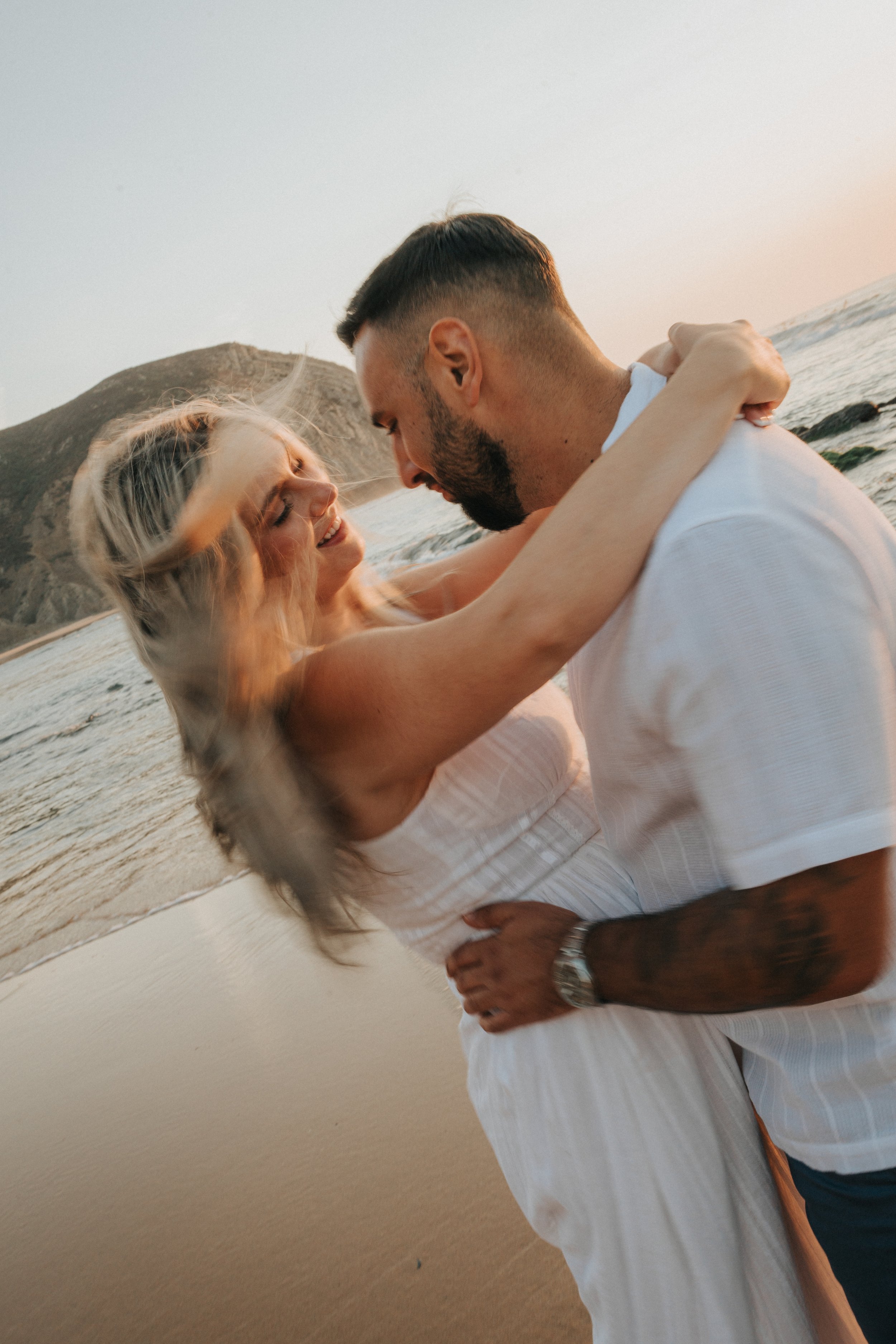 A couple dancing on the beach at sunset, with mountains in the background.