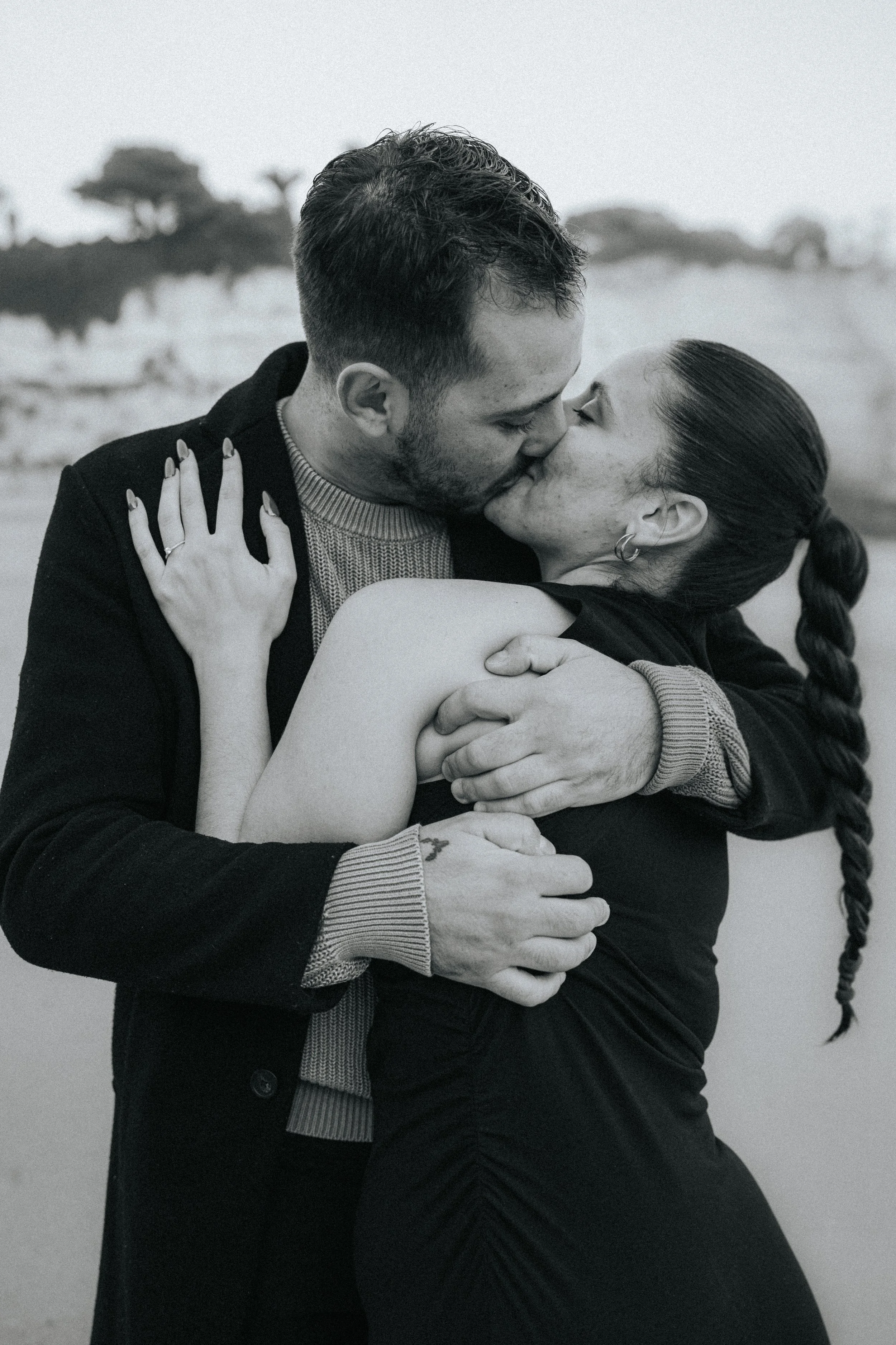 A couple kissing on a beach, with the woman embracing the man and both smiling over their embrace.
