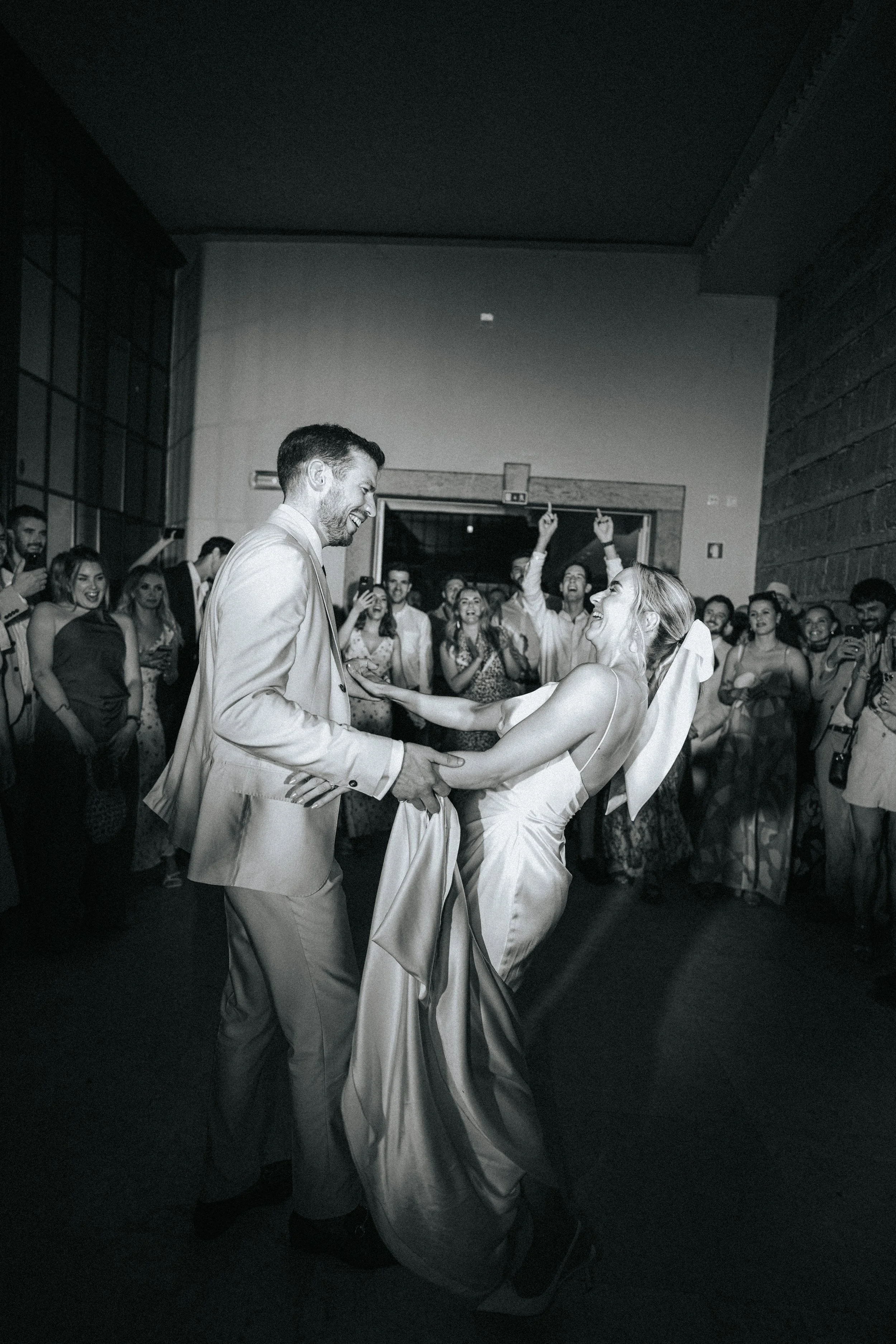 A bride and groom dancing at their wedding reception, surrounded by guests who are smiling and celebrating.