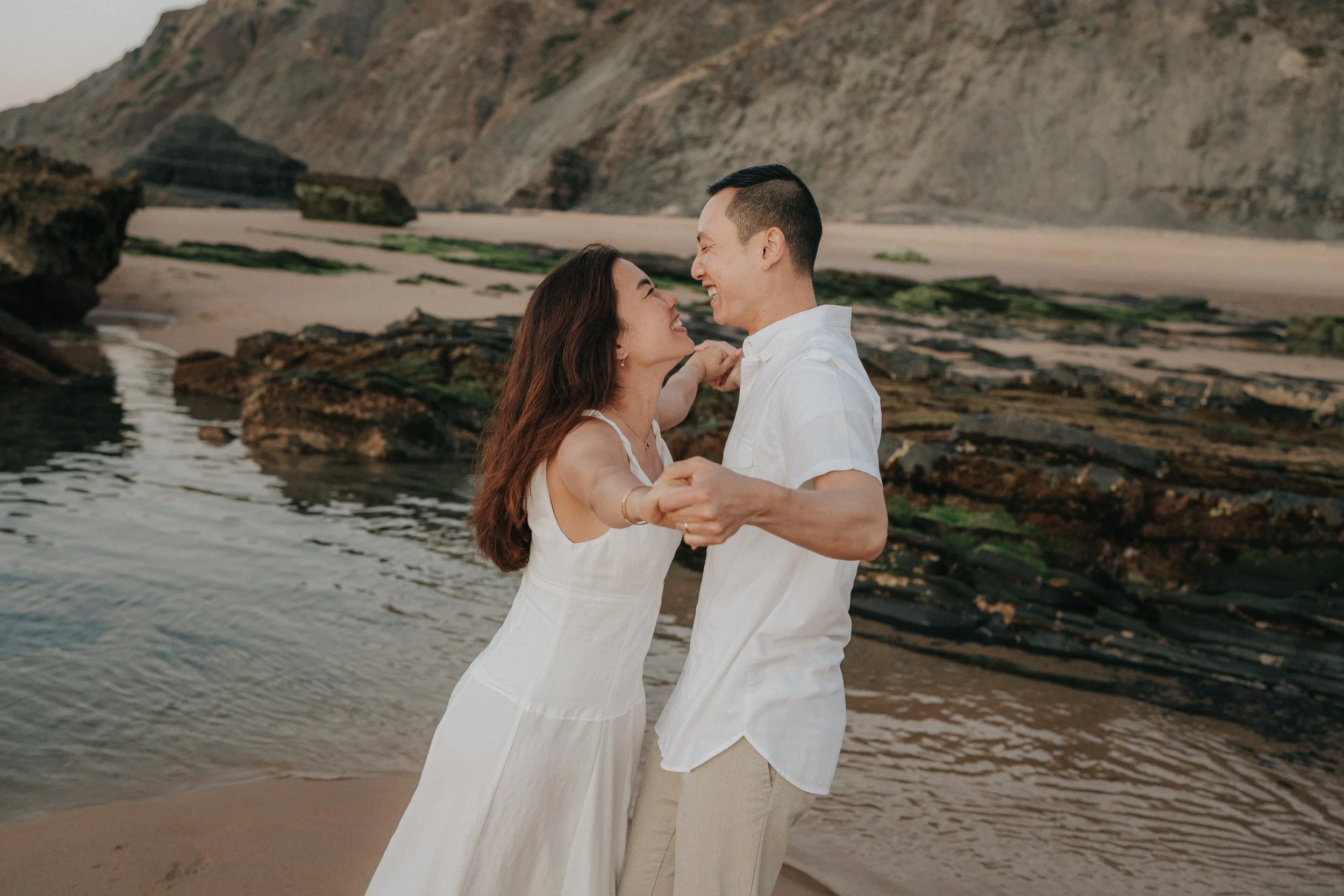 A happy couple dancing on the beach with rocky cliffs in the background