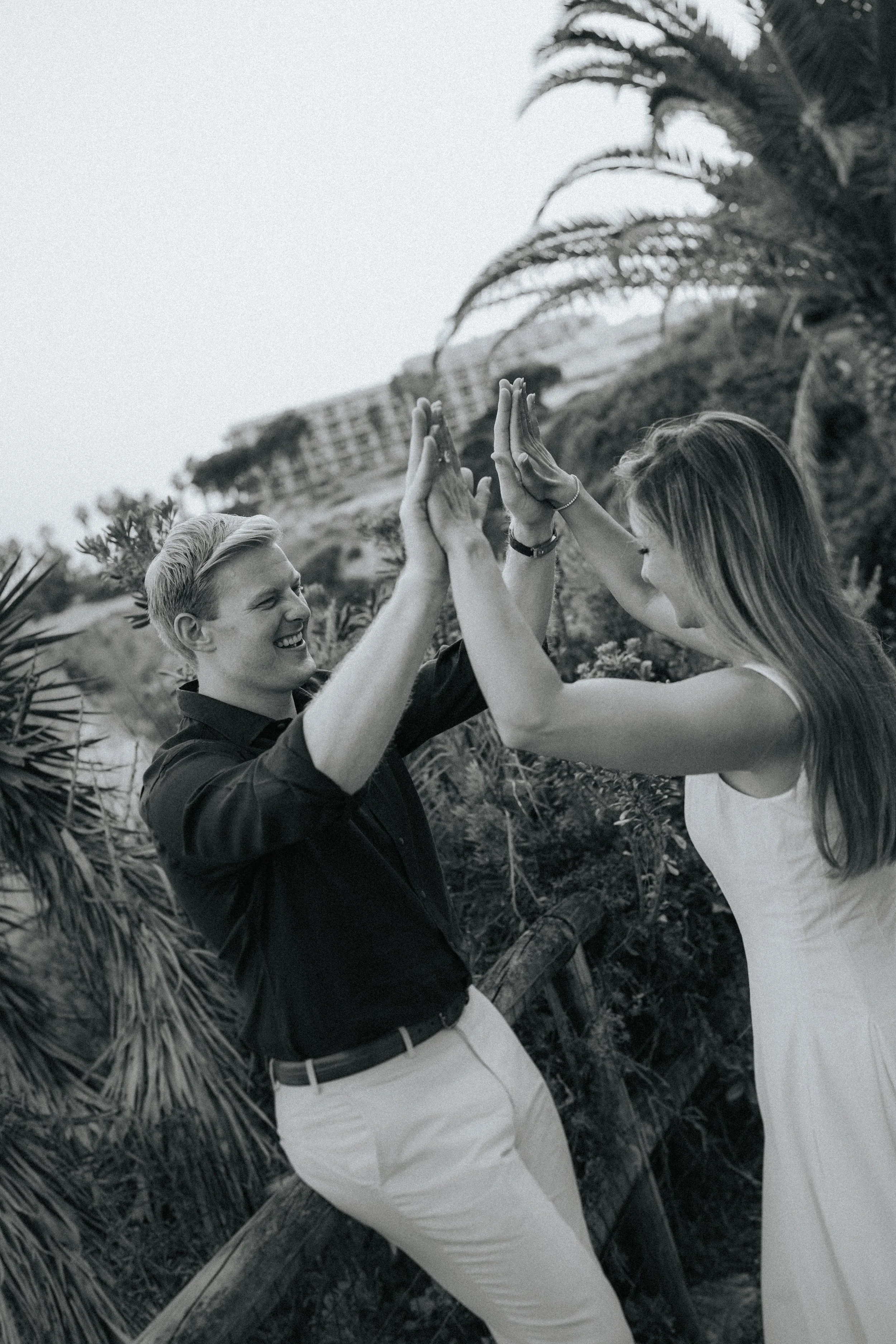A smiling man and woman high-fiving outdoors among tropical plants and trees.