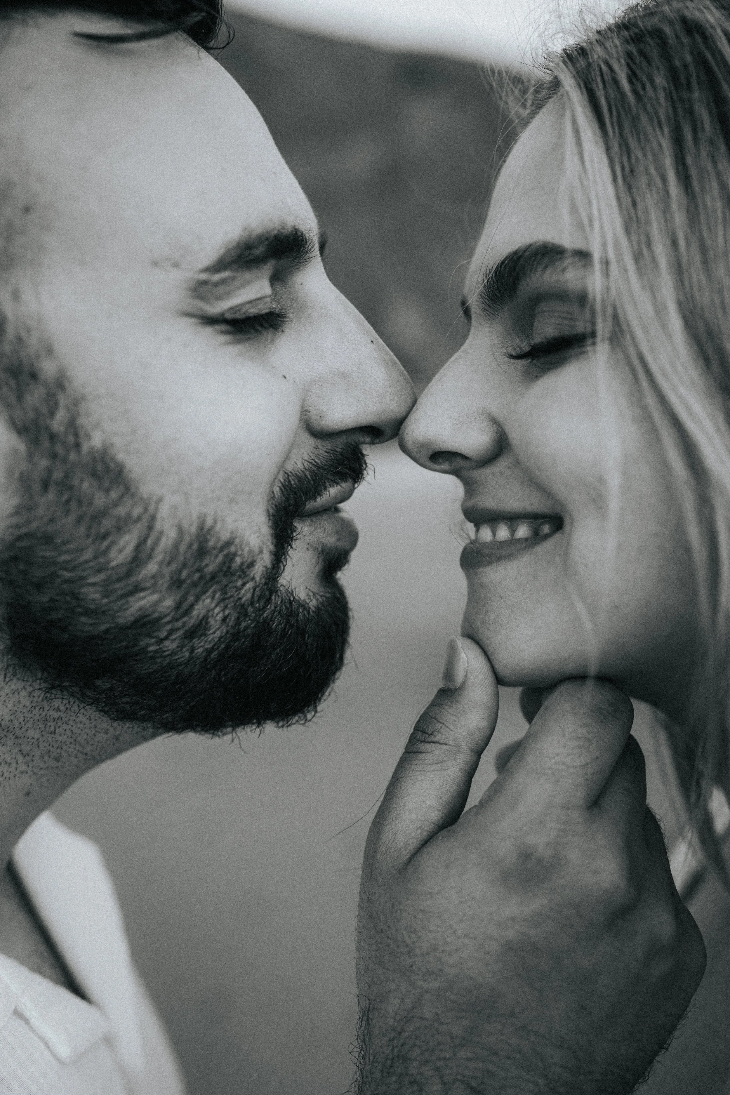 A close-up black and white photo of a man and woman touching foreheads and smiling with eyes closed, showing intimacy and affection.