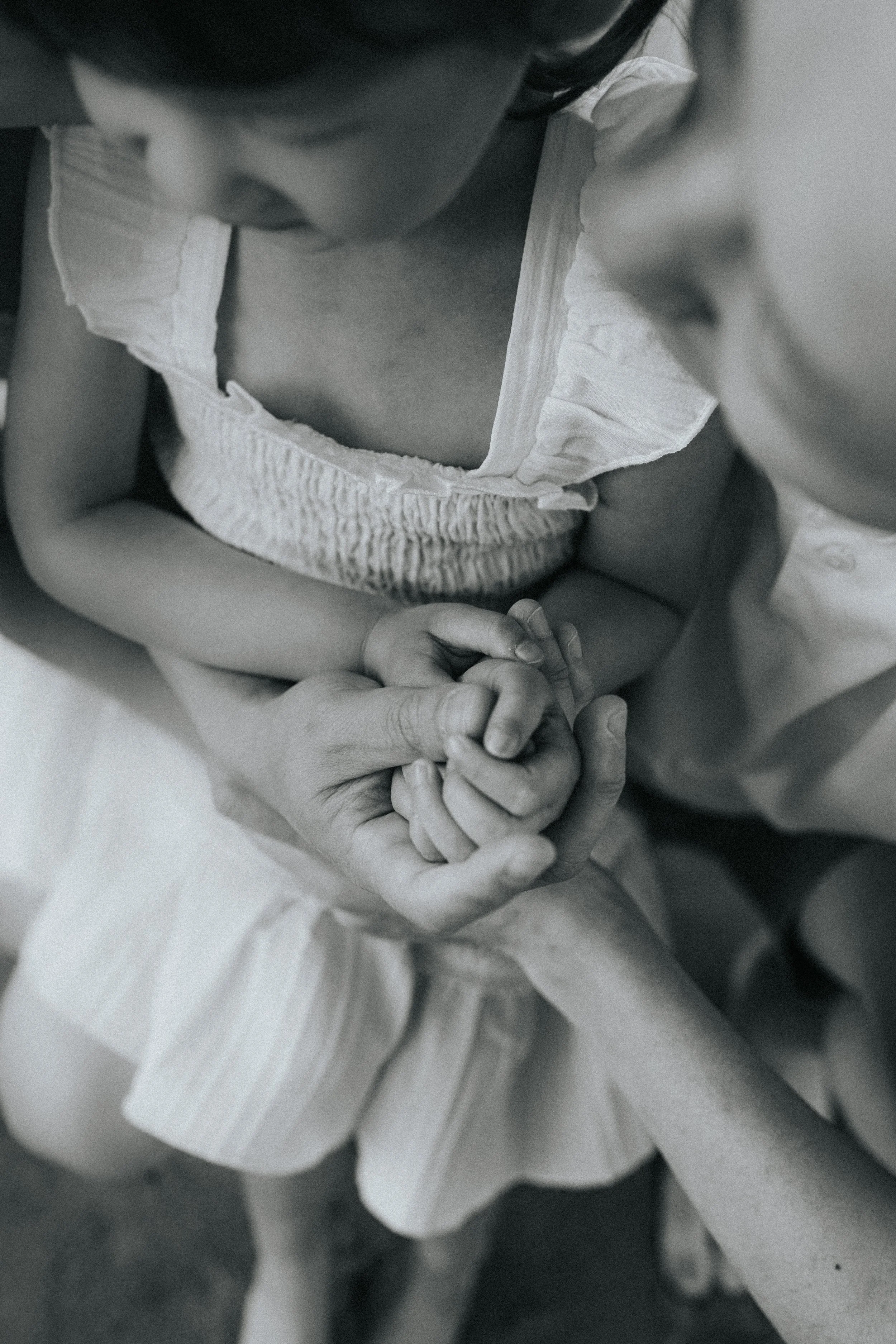 Close-up of a child's hands clasped together, with part of the child's face and body visible in a soft, black and white photo.