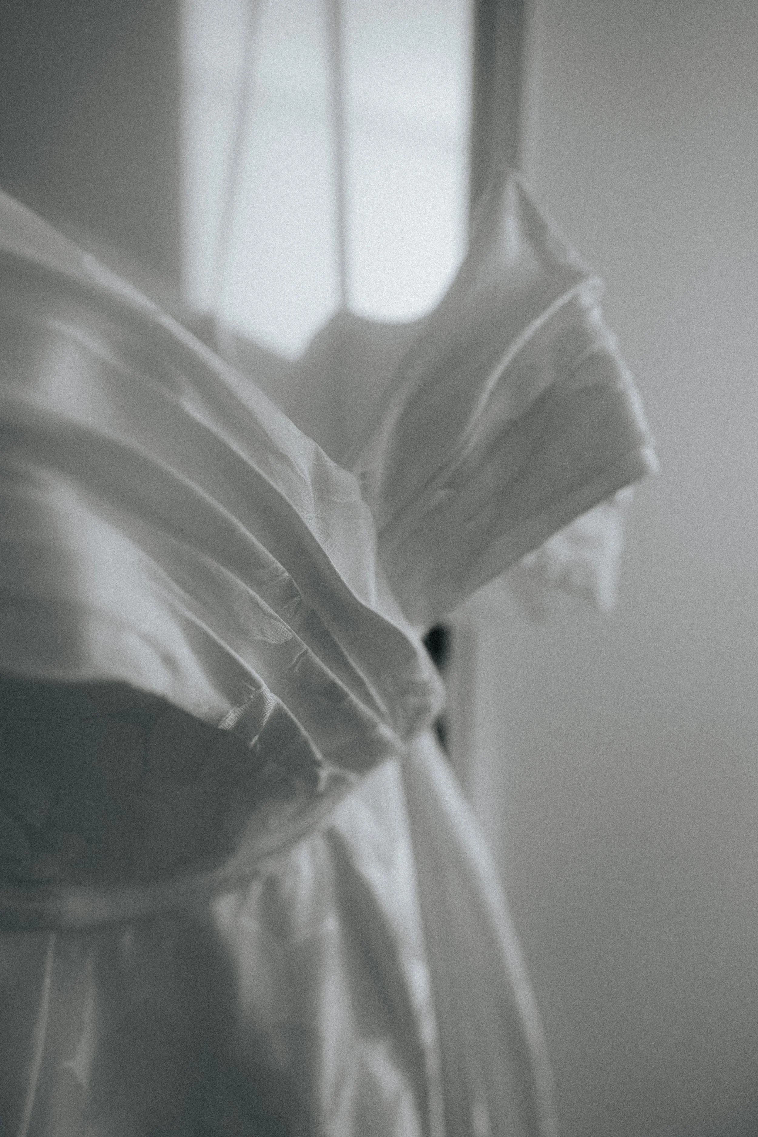 A person wearing a striped shirt lifting a folded white garment or fabric.