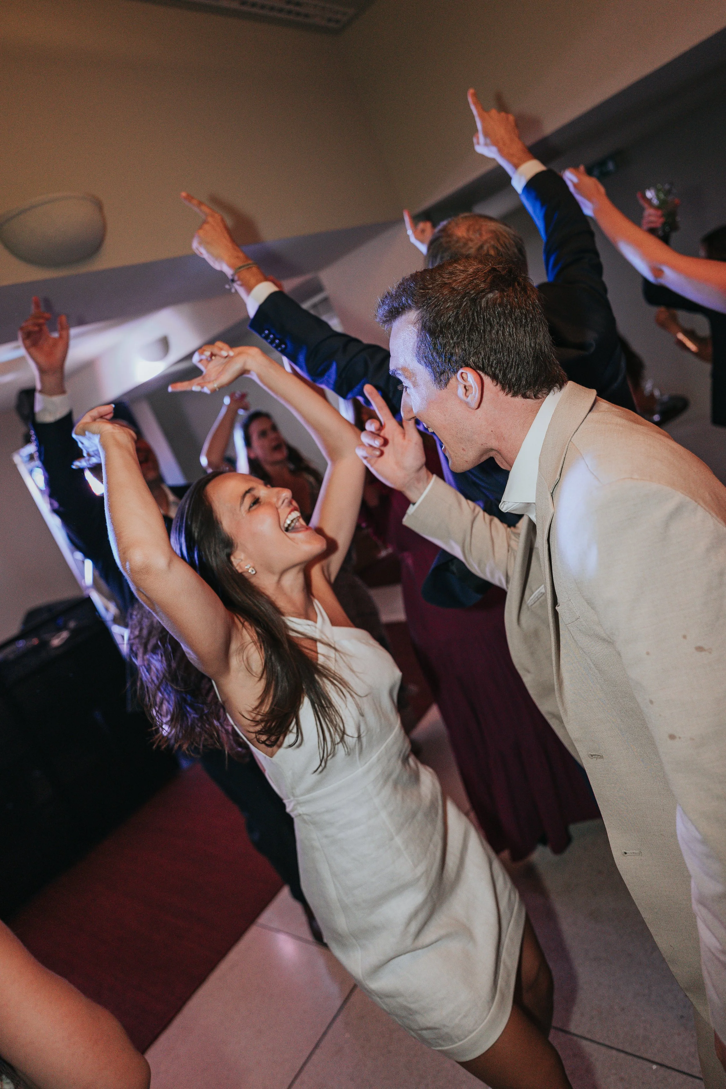 People dancing at a celebration or party, with some raising their arms and smiling.