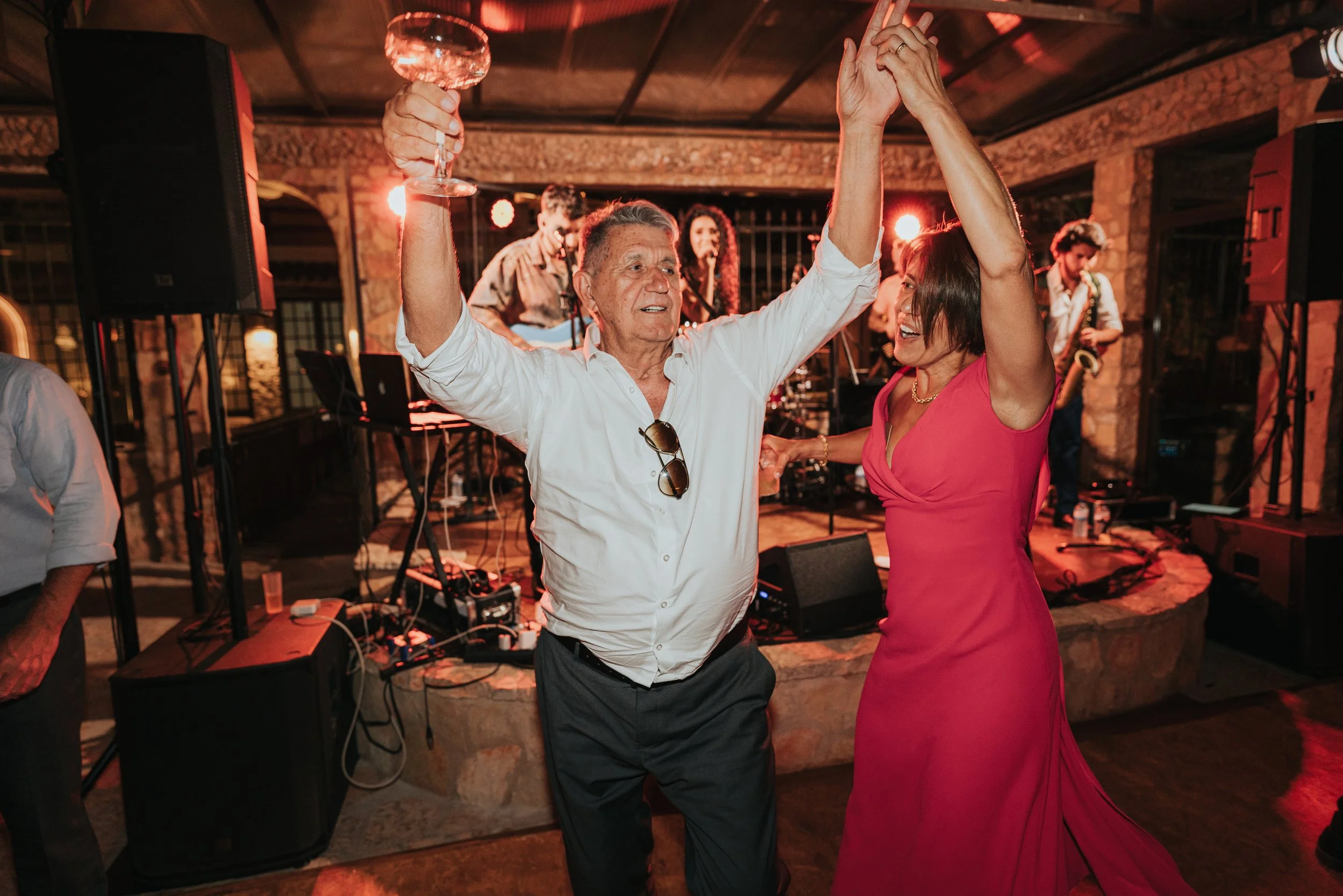 An elderly man and woman dancing together in a lively setting with a live band playing in the background.