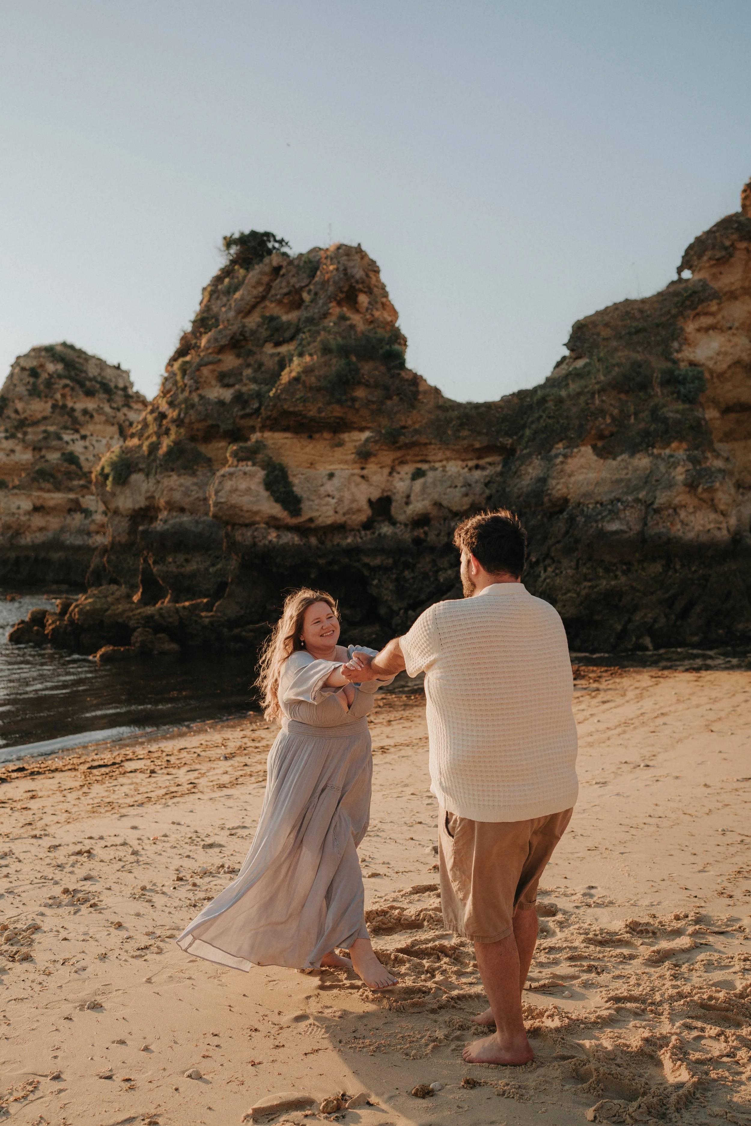 A couple dancing on a beach at sunset, with rocky cliffs in the background.