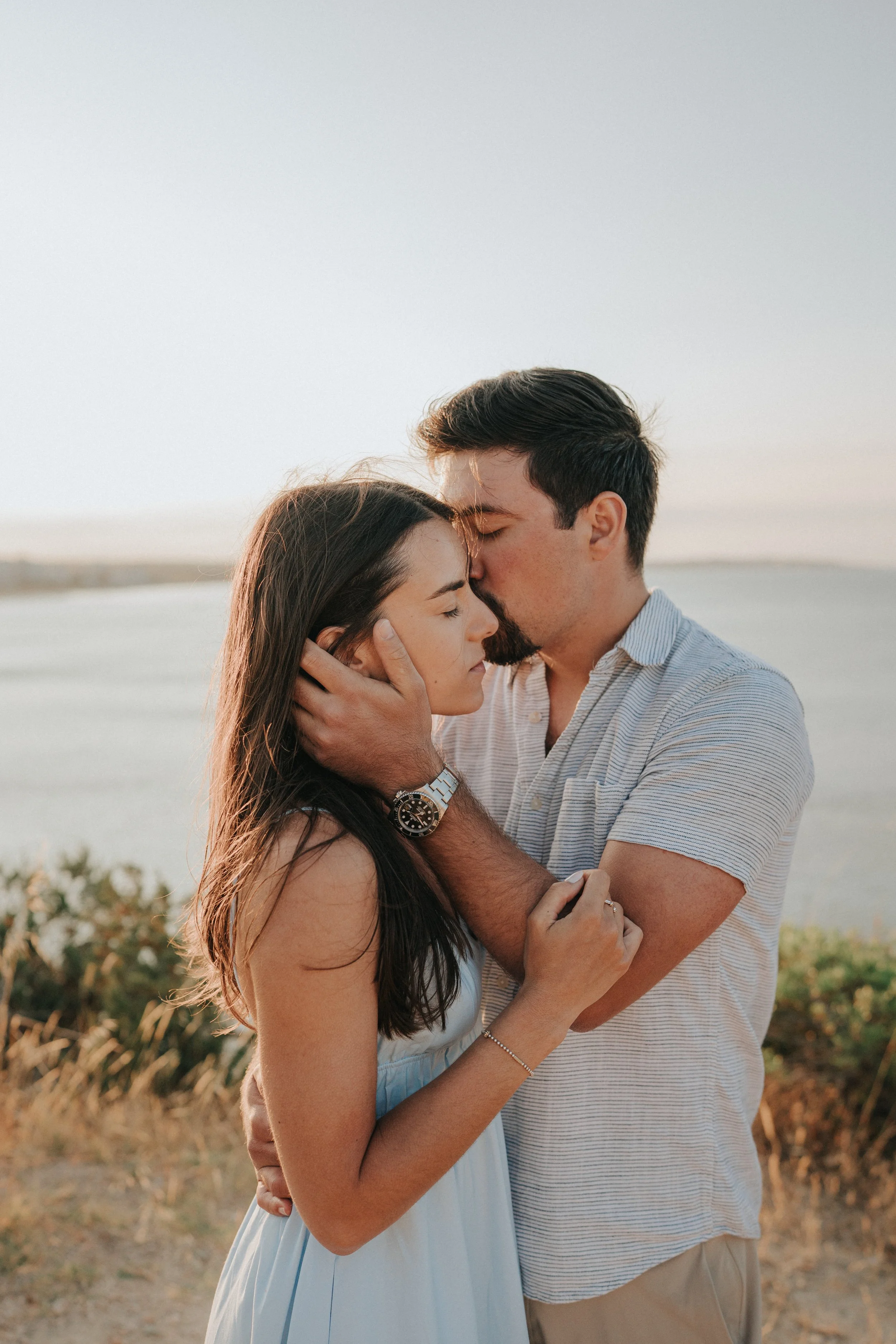 A young couple shares a close, intimate moment at sunset outdoors, with the man holding the woman's face gently.