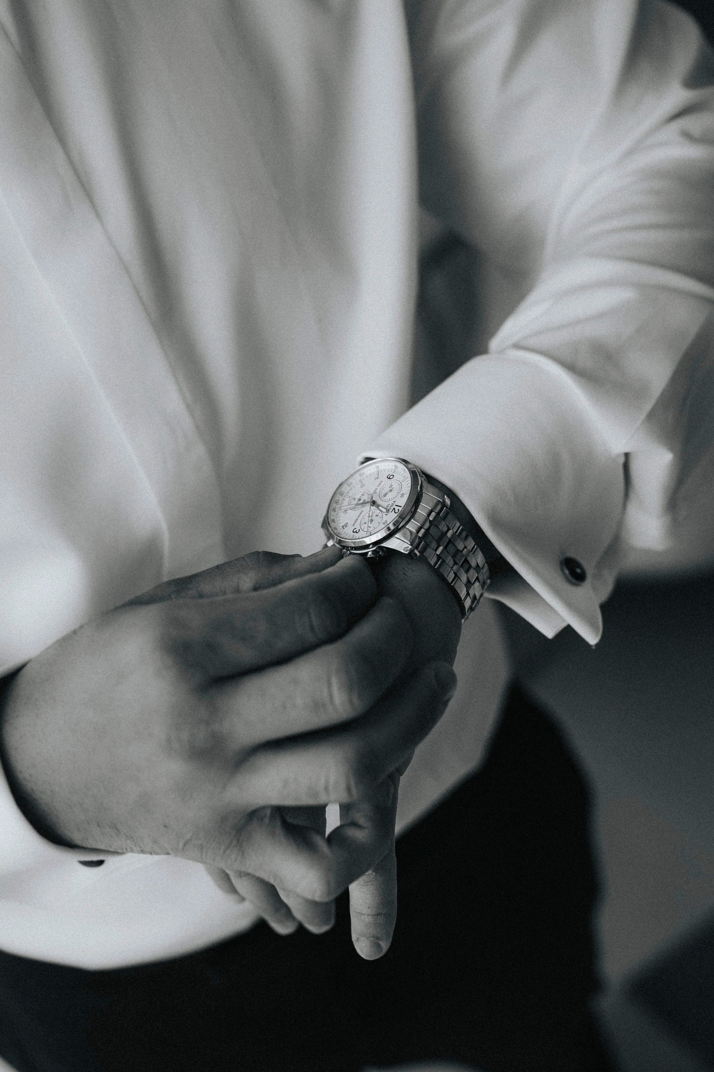 A close-up of a person in formal attire adjusting a wristwatch on another person's wrist, both wearing white shirts.