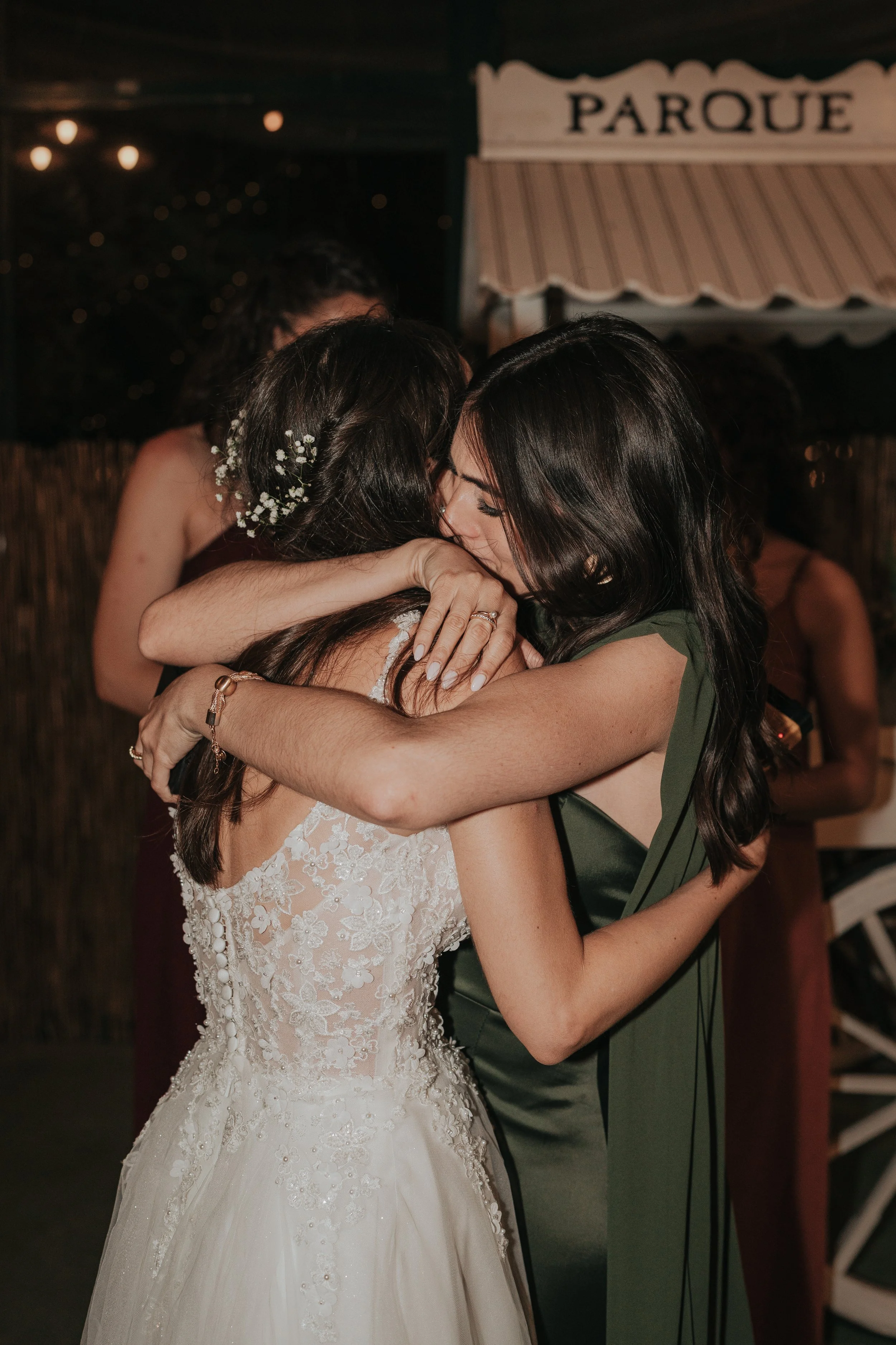 Two women hugging tightly at a celebration event, with one wearing a bridal gown and the other in a green dress.