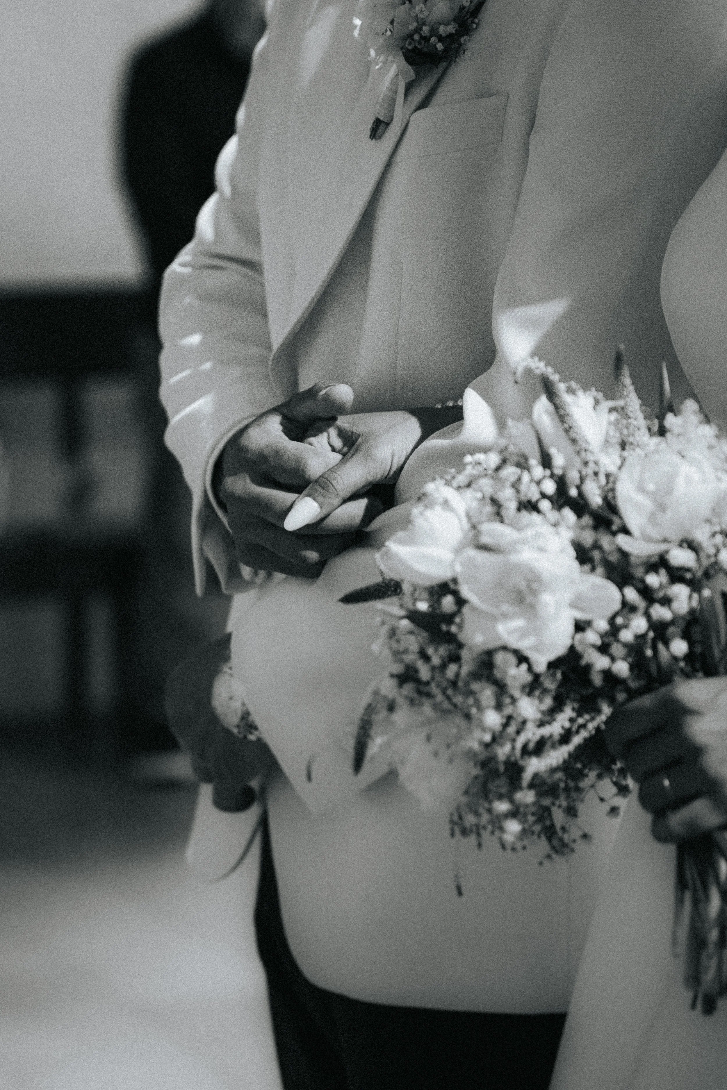 Close-up of a person holding a bouquet of flowers, wearing a white jacket and black pants.