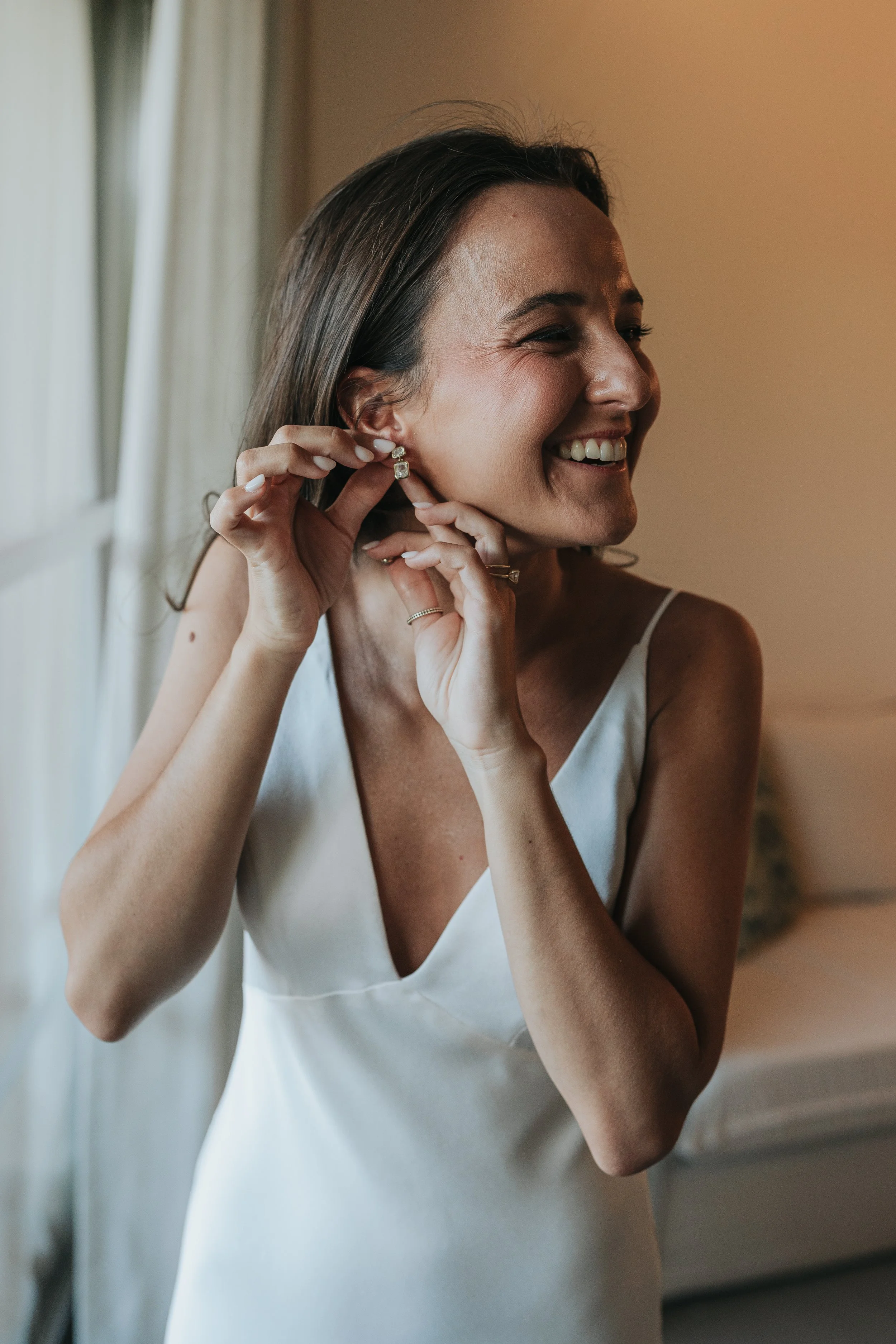 A woman smiling while putting on a pair of elegant earrings.