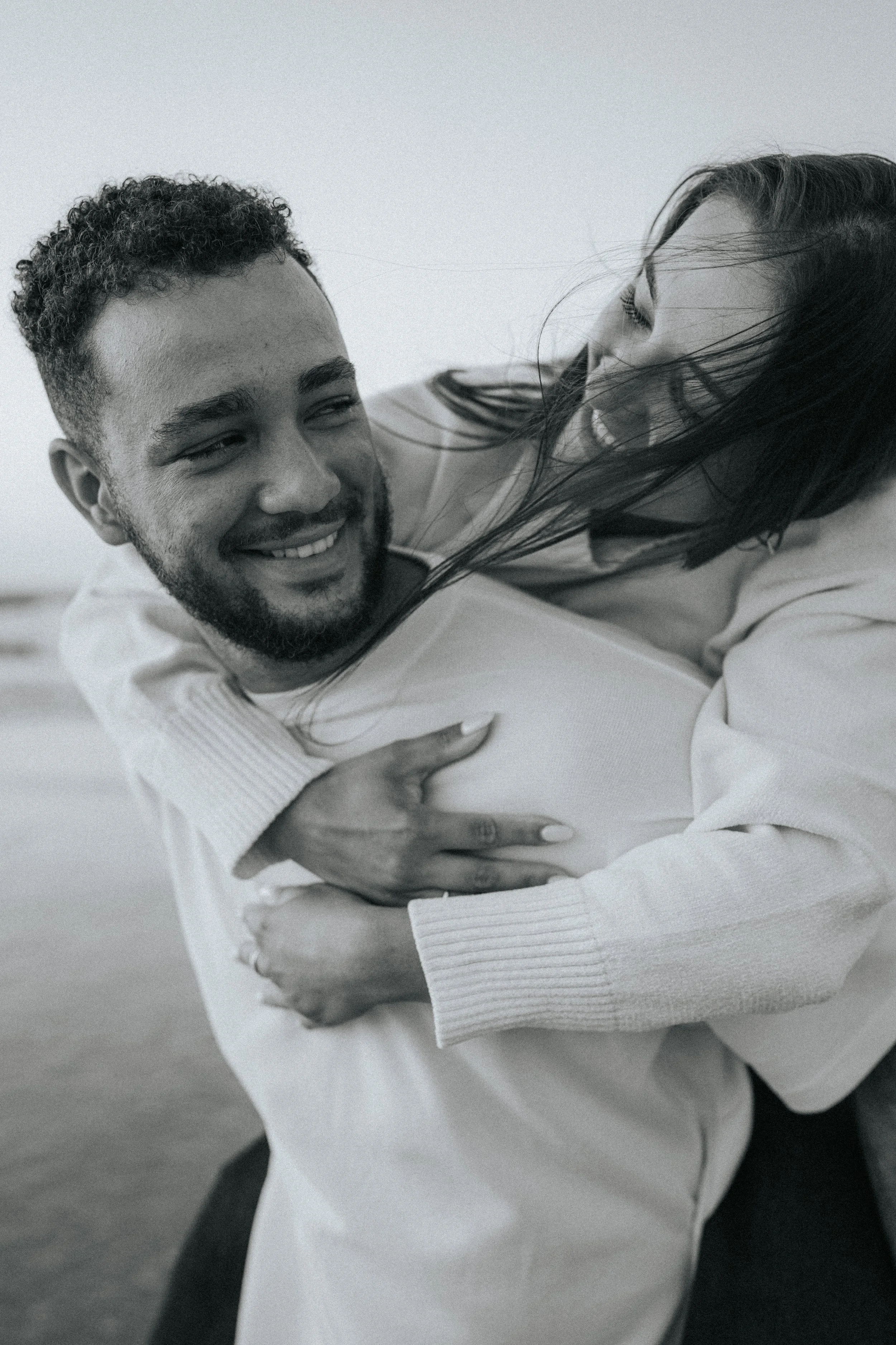 Two people engaging in a playful, affectionate embrace, smiling and laughing together indoors.