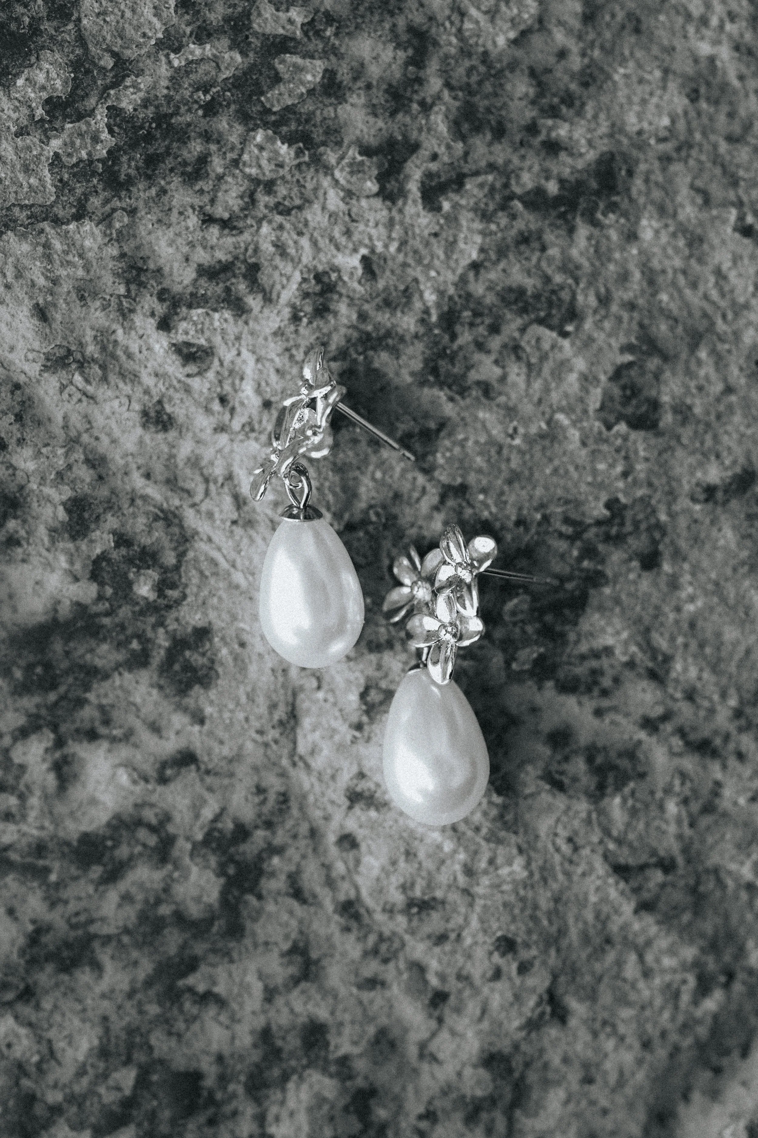 Close-up of a pair of silver earrings with white teardrop-shaped stones hanging against a textured gray stone background.