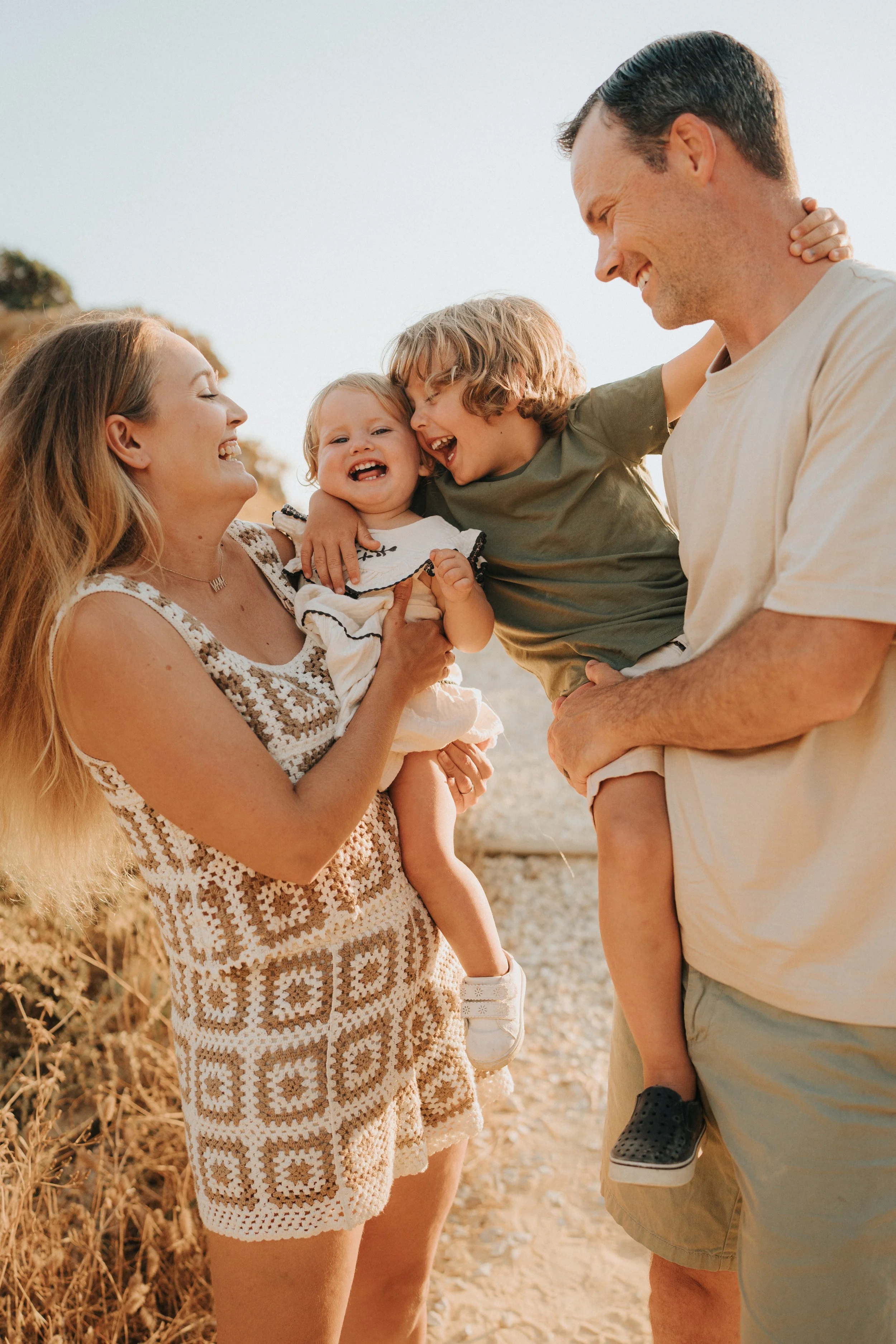 A family of four enjoying a moment outdoors, two children and two adults, smiling and interacting on a sunny day with natural outdoor background.