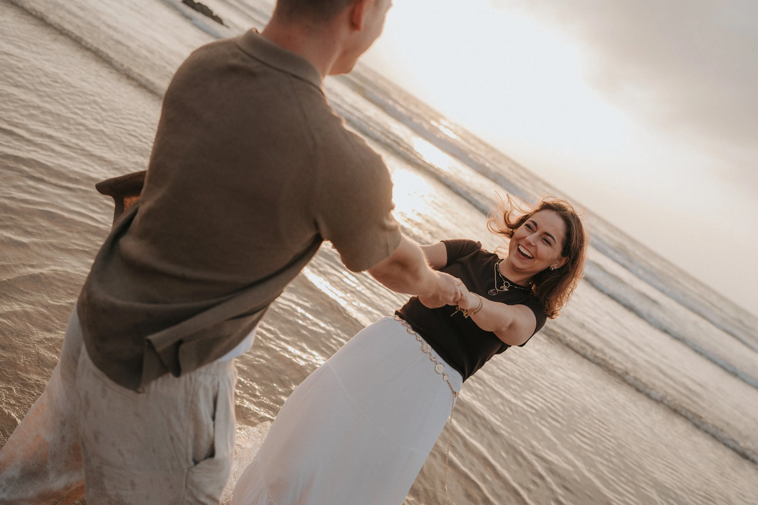 A man and a woman on the beach at sunset, holding hands and smiling at each other.