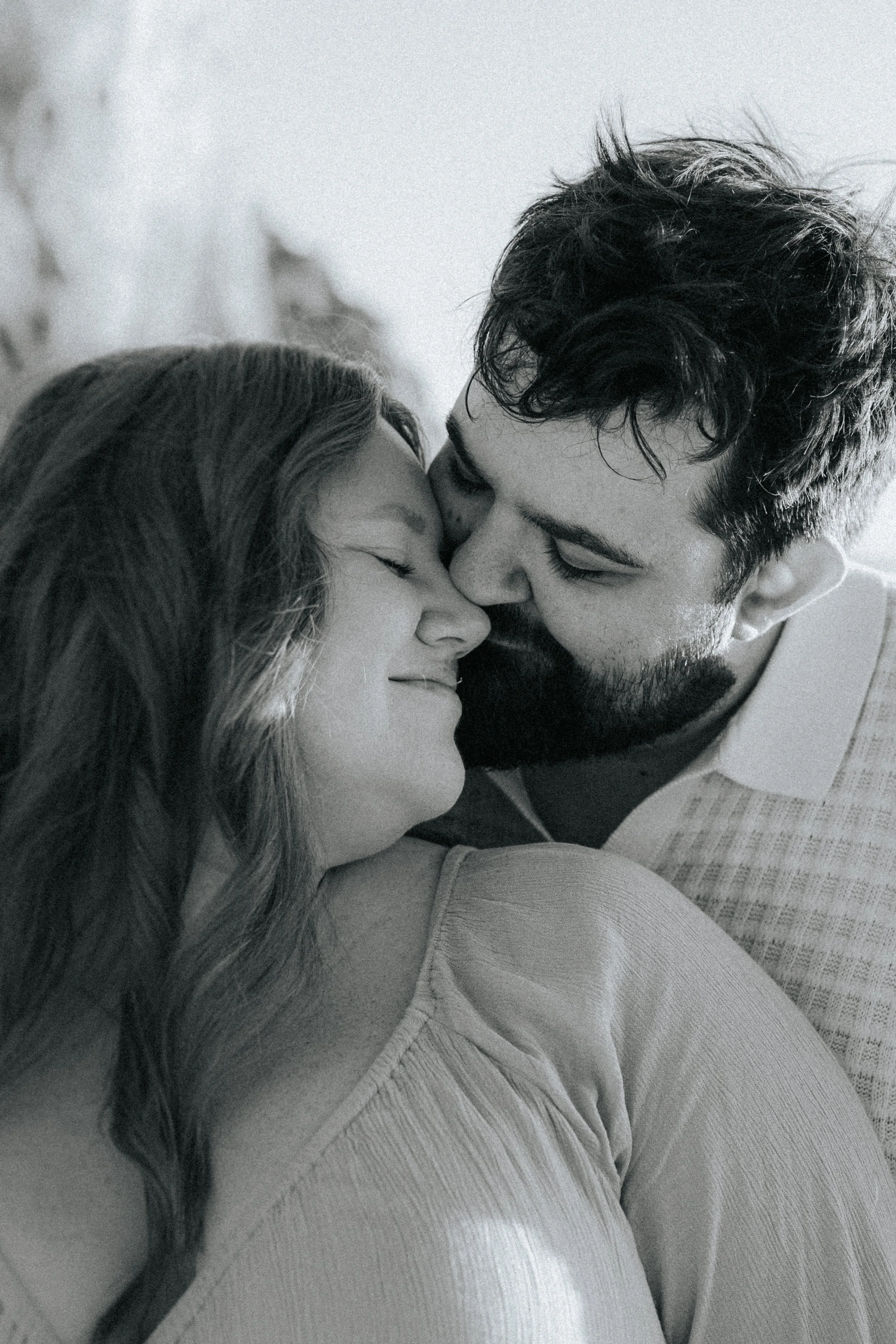 A black-and-white photograph of a couple with their foreheads touching and eyes closed, conveying intimacy and affection.