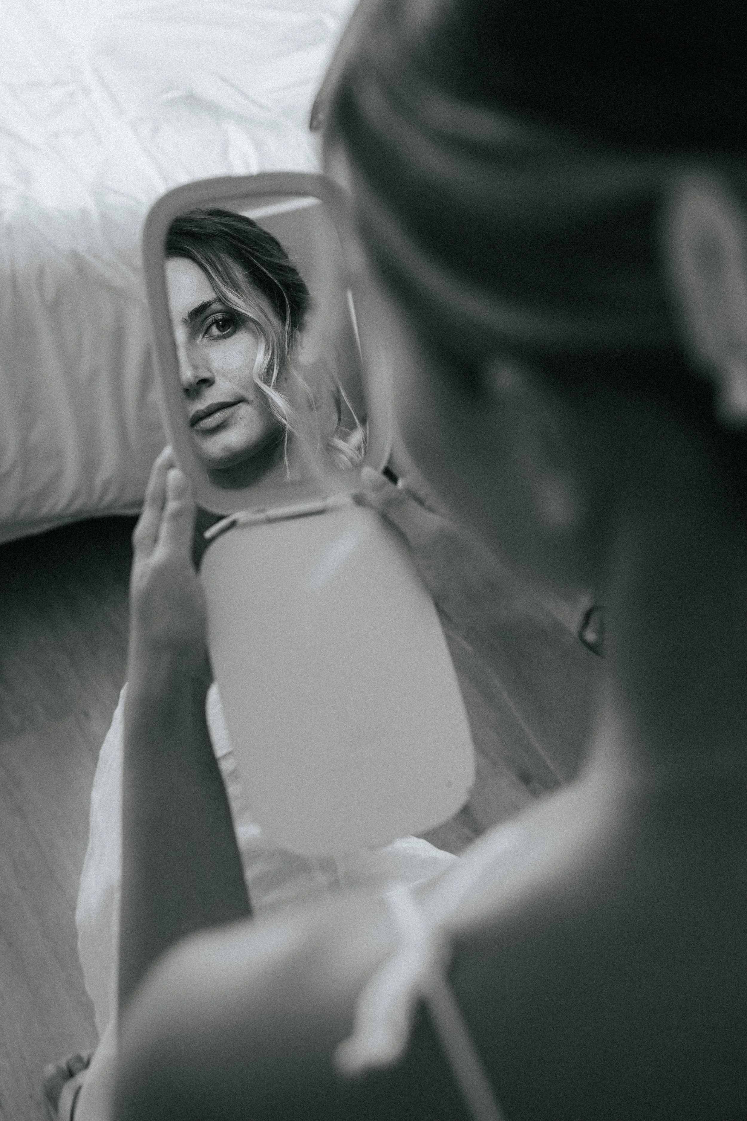 A person holding a mirror reflects a woman's face as she looks at herself with a gentle expression.