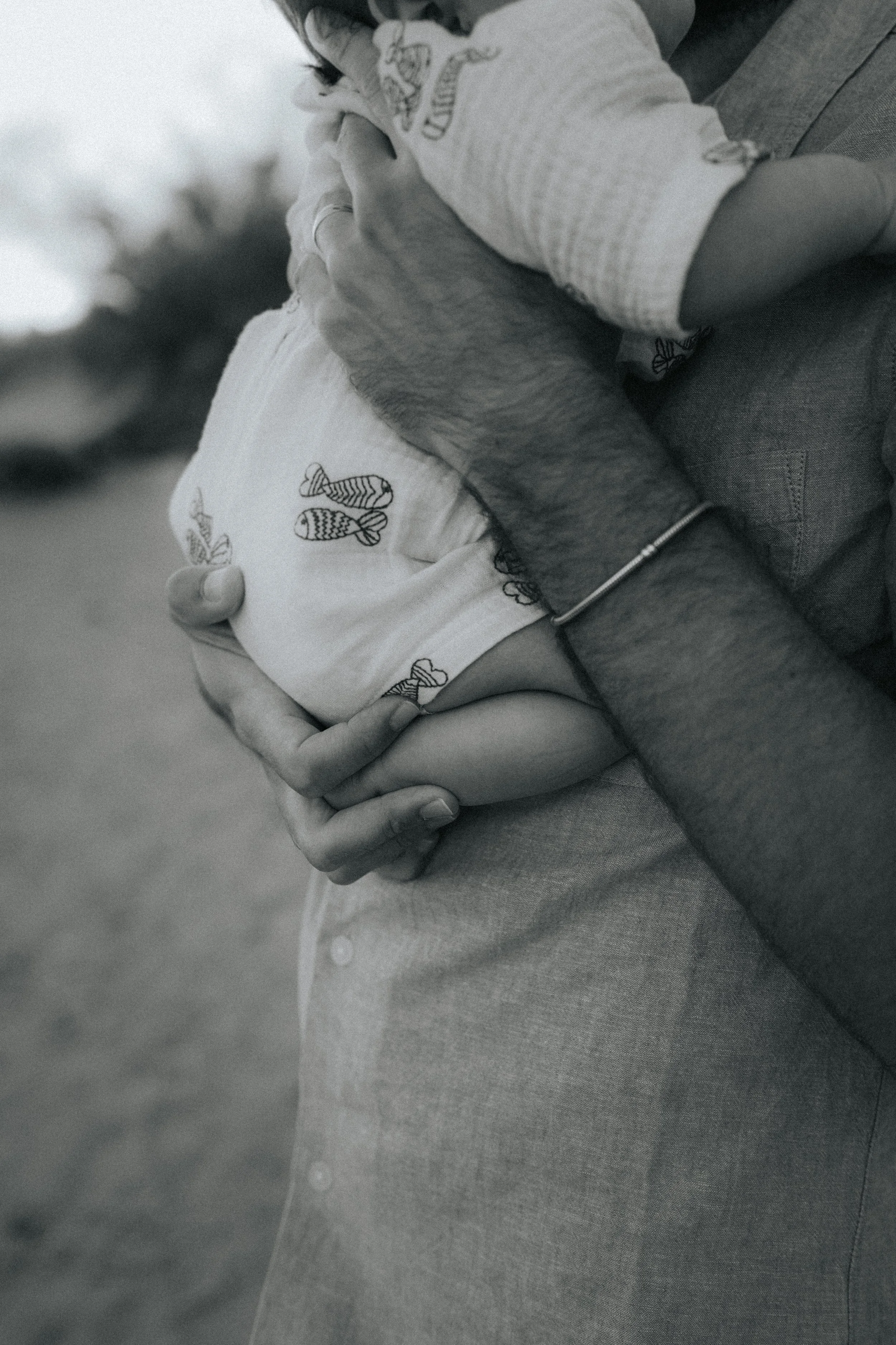 A person holding a baby wearing a hat with fish pattern. The adult's hand is gently holding the baby, and the baby is cradled in the caregiver's arms.