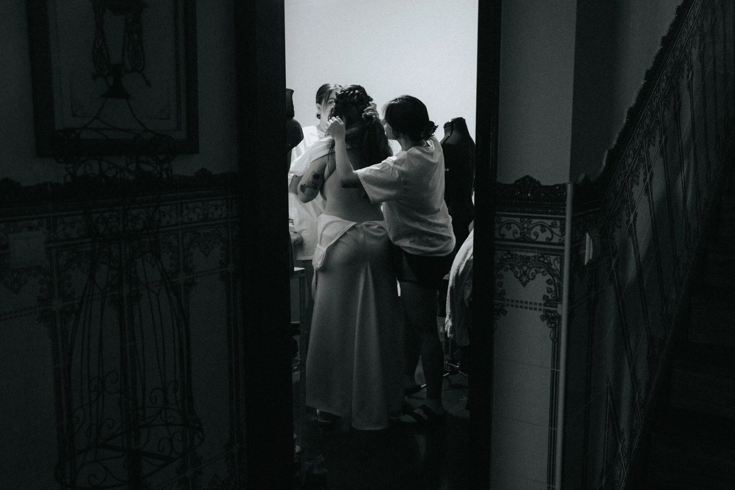 A black and white photo of a woman with long hair, two people in medical gowns, possibly nurses, crouched near her, likely in a medical or intimate setting.