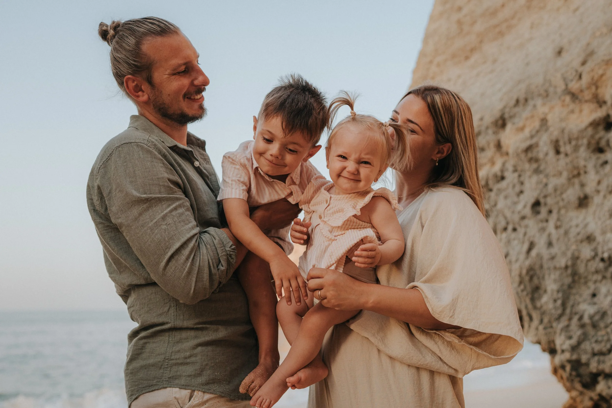 A family of four standing on a beach with cliffs in the background, smiling and enjoying their time together.