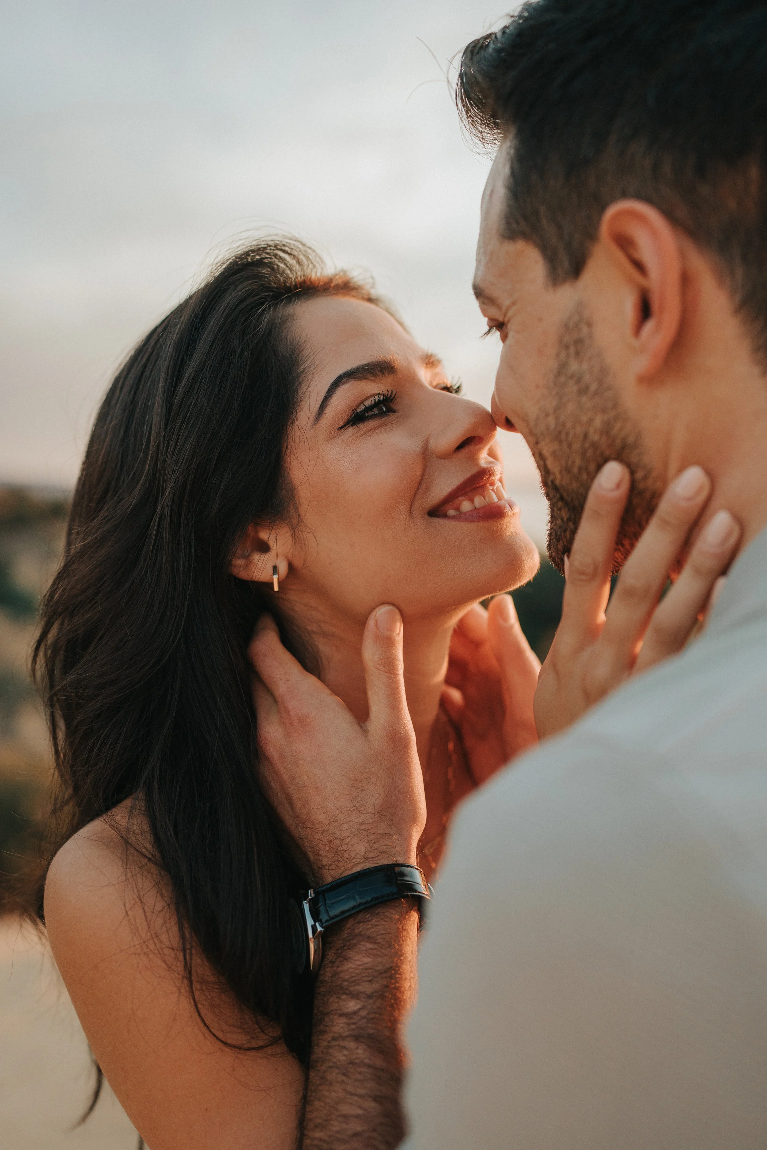 A close-up of a couple touching foreheads, gazing into each other's eyes, outdoors during sunset.