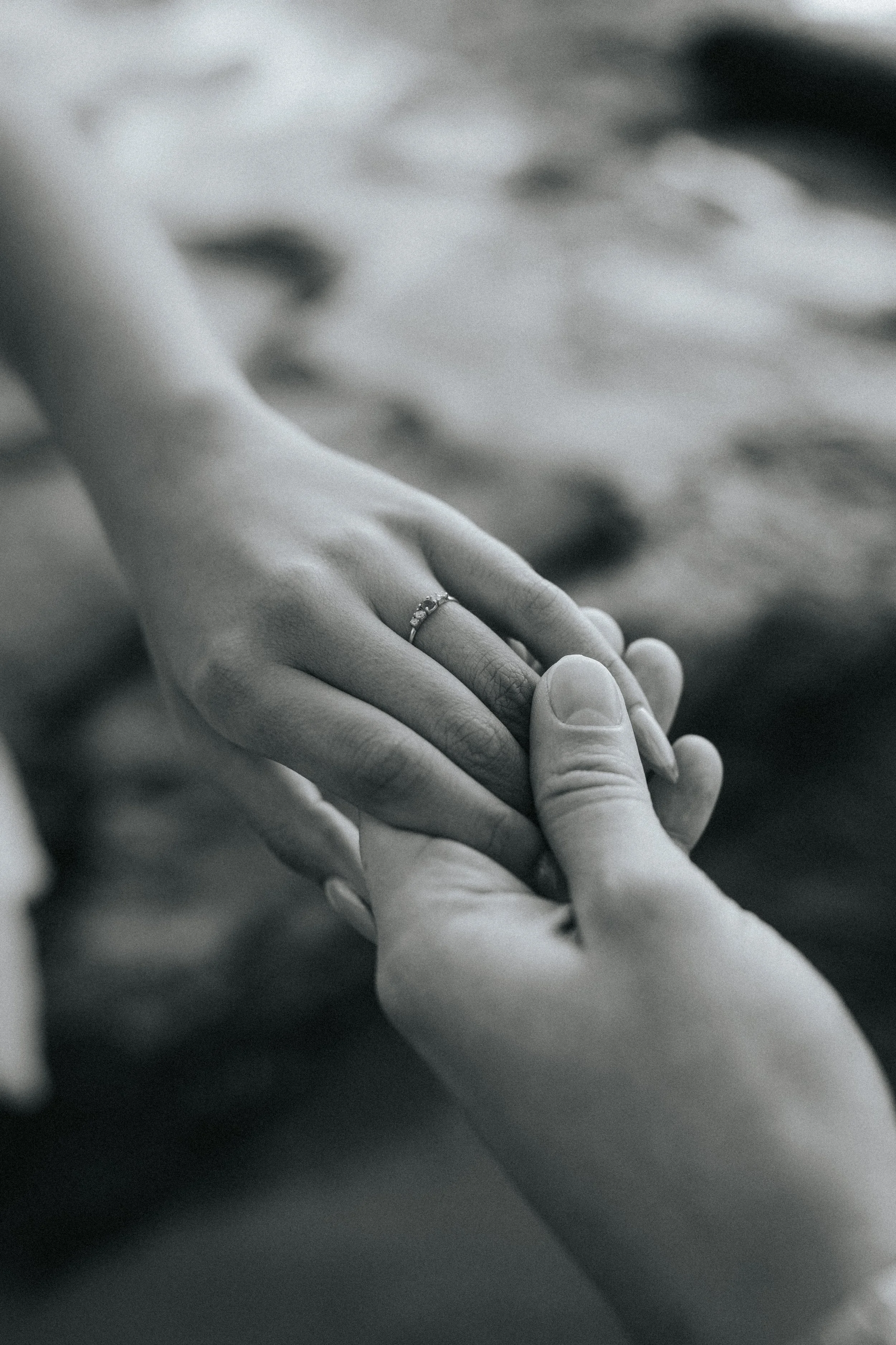 Close-up of two hands gently holding each other, one hand with a ring on the ring finger, in black and white.