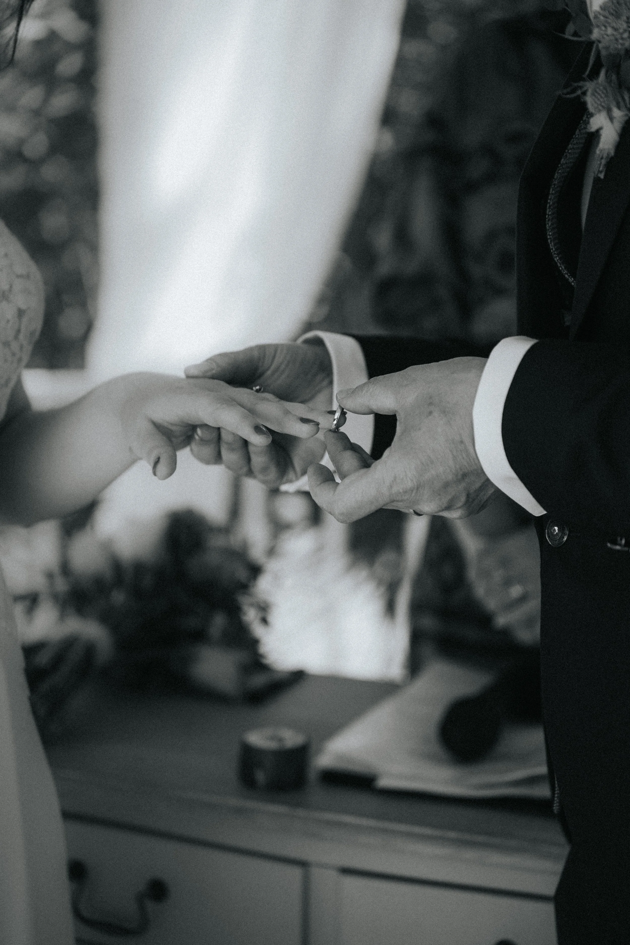 A person in a suit placing a ring on a woman's finger during a wedding ceremony.