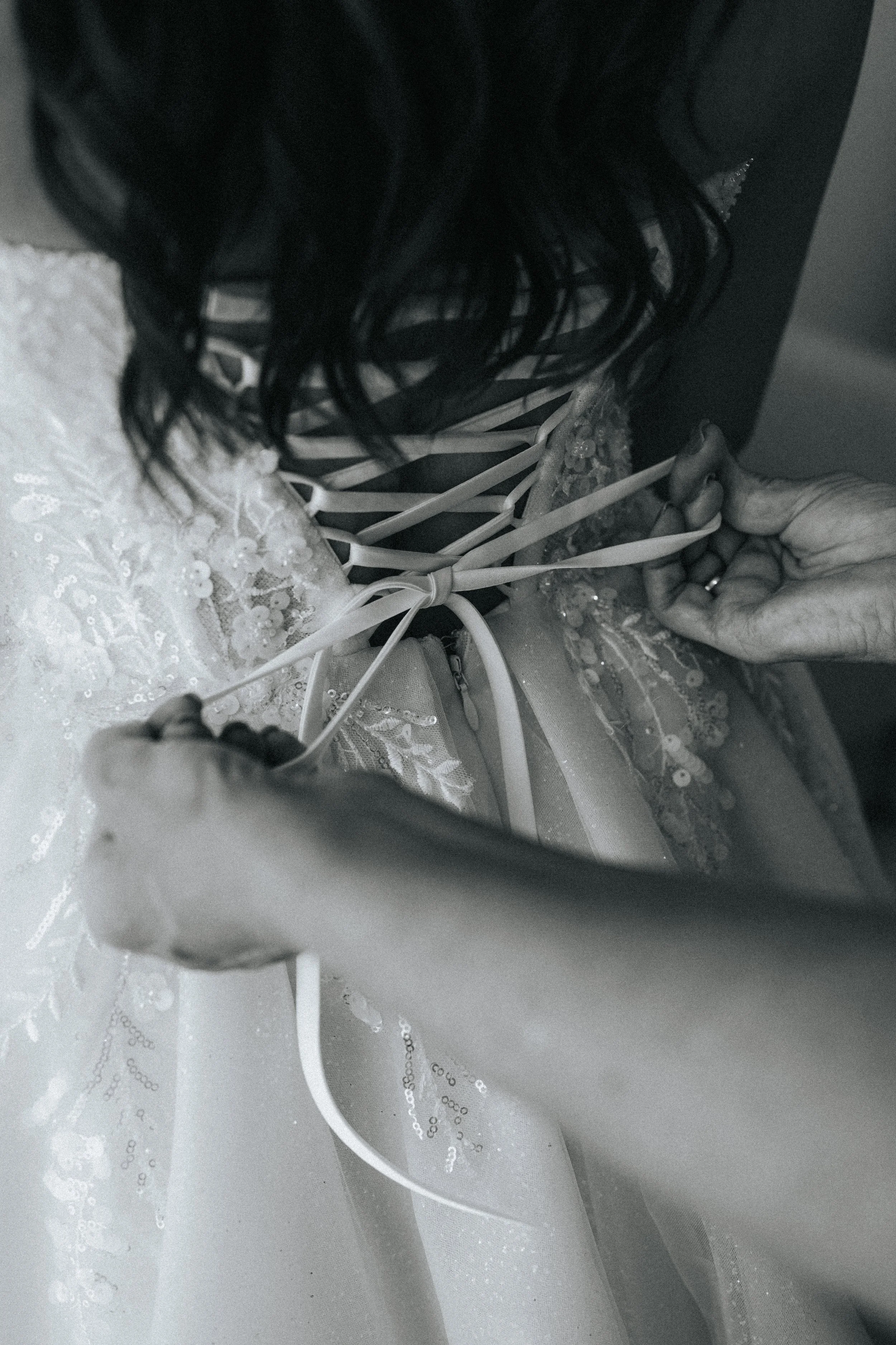 A person with dark hair wearing a lacy dress is tying a ribbon on a decorative item, possibly a wedding or special occasion decoration, on a table with a white, sequined or embroidered fabric.