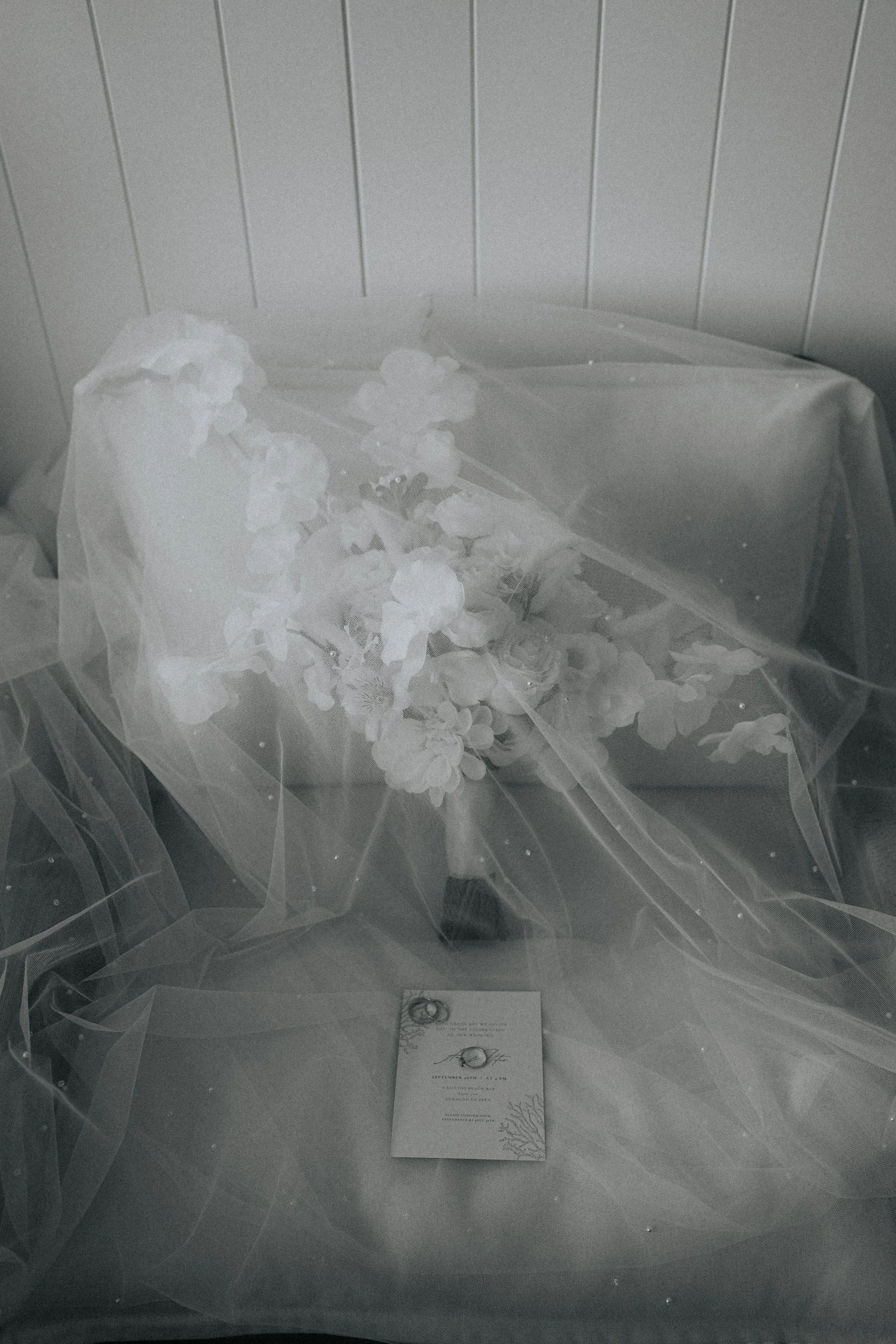 A wedding or engagement announcement card placed inside a transparent plastic bag, with decorative flowers and rings nearby.