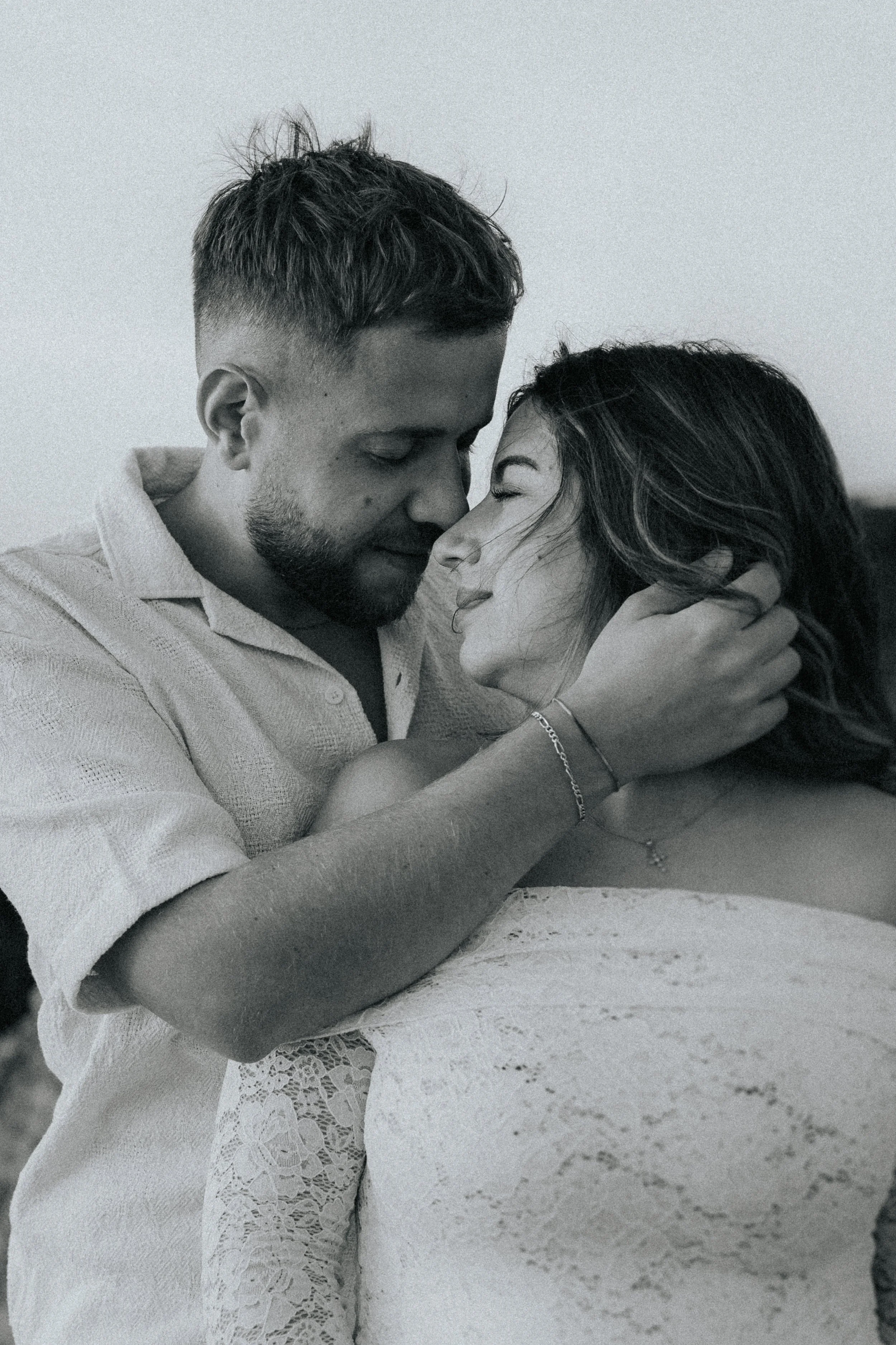 A black and white photo of a couple embracing with their foreheads touching, eyes closed, displaying affection and intimacy.