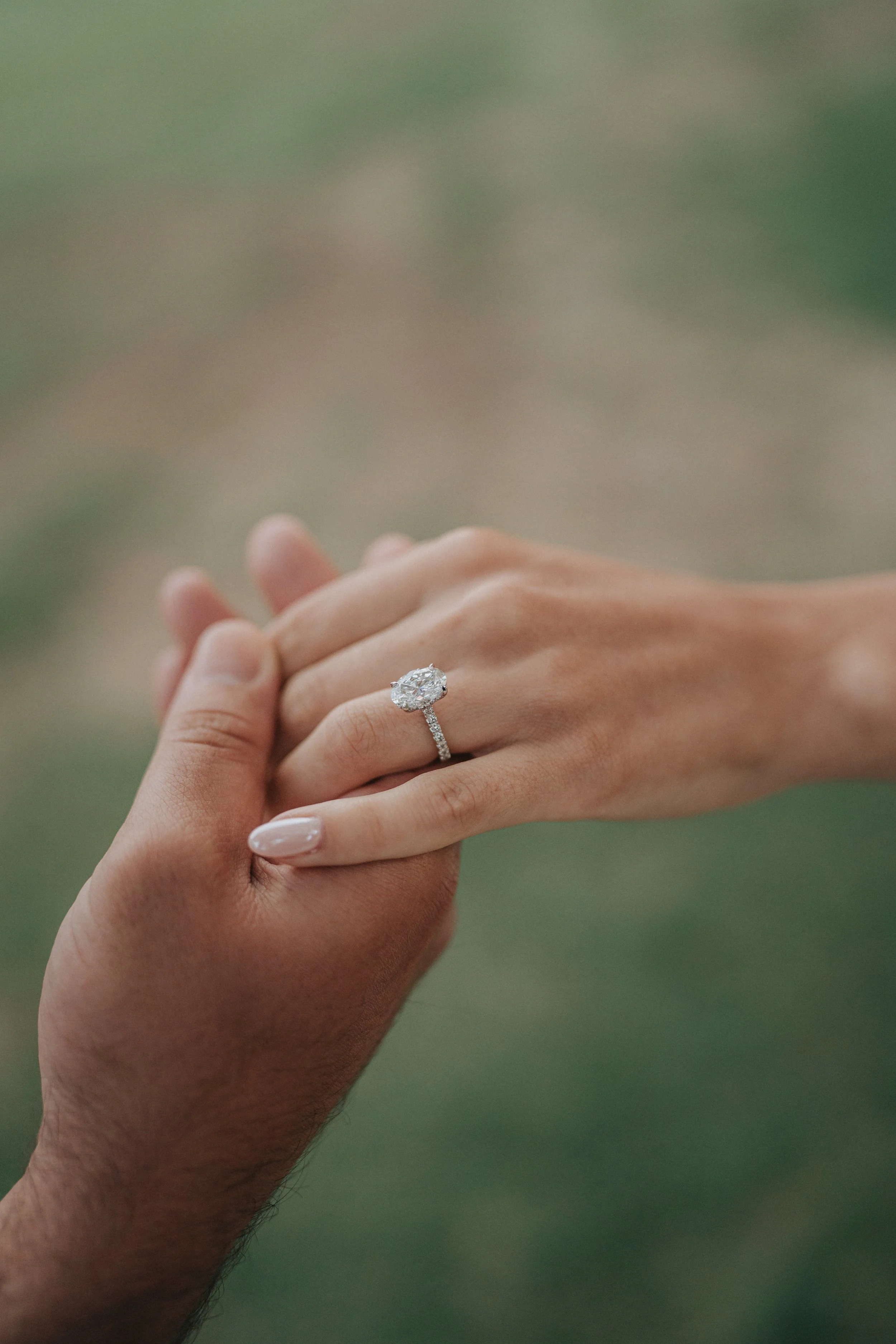 A close-up of two hands holding each other, one hand has a large diamond engagement ring on the ring finger.