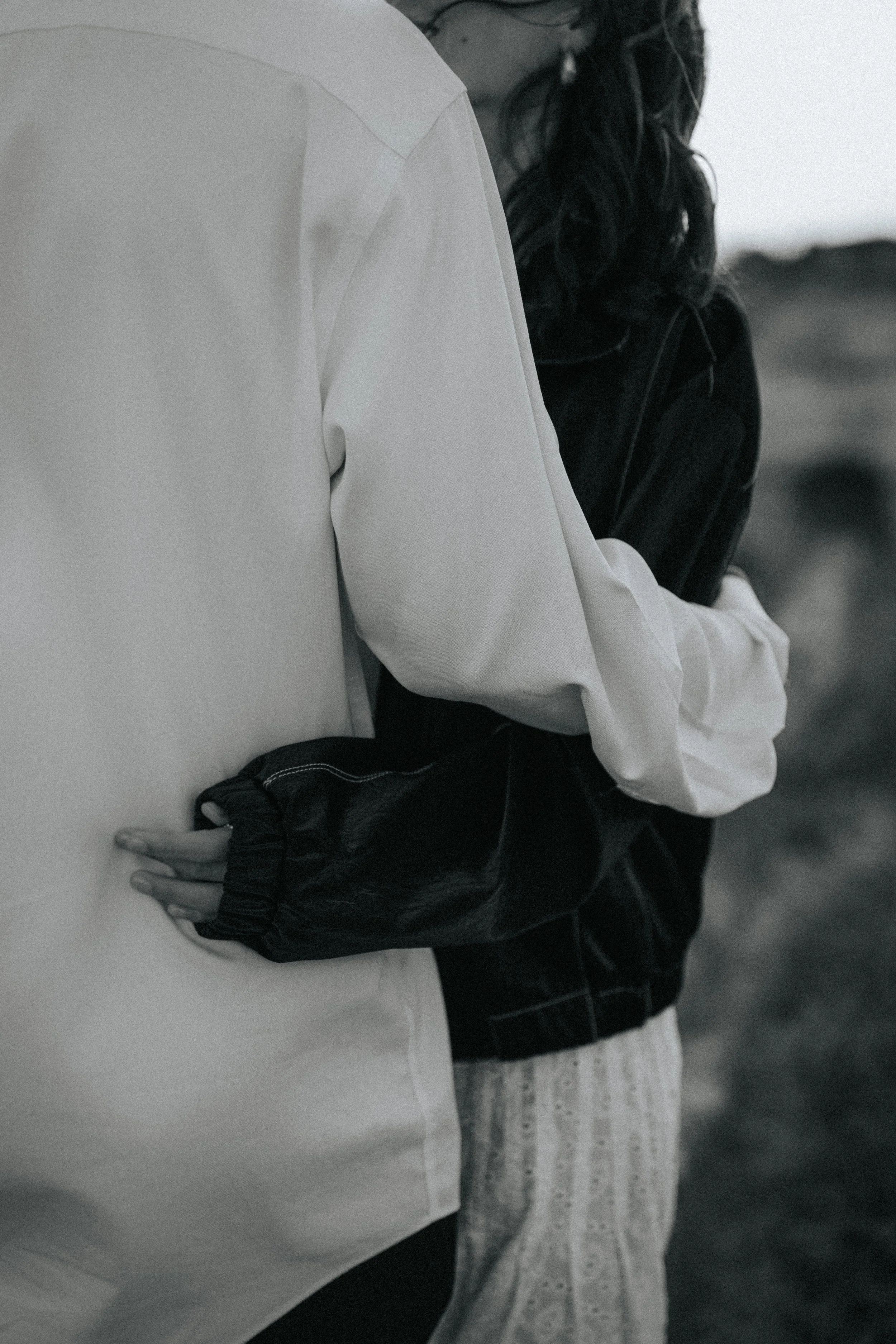 Close-up of two people embracing, one wearing a white shirt and the other wearing a black jacket and a patterned skirt, with their arms wrapped around each other.