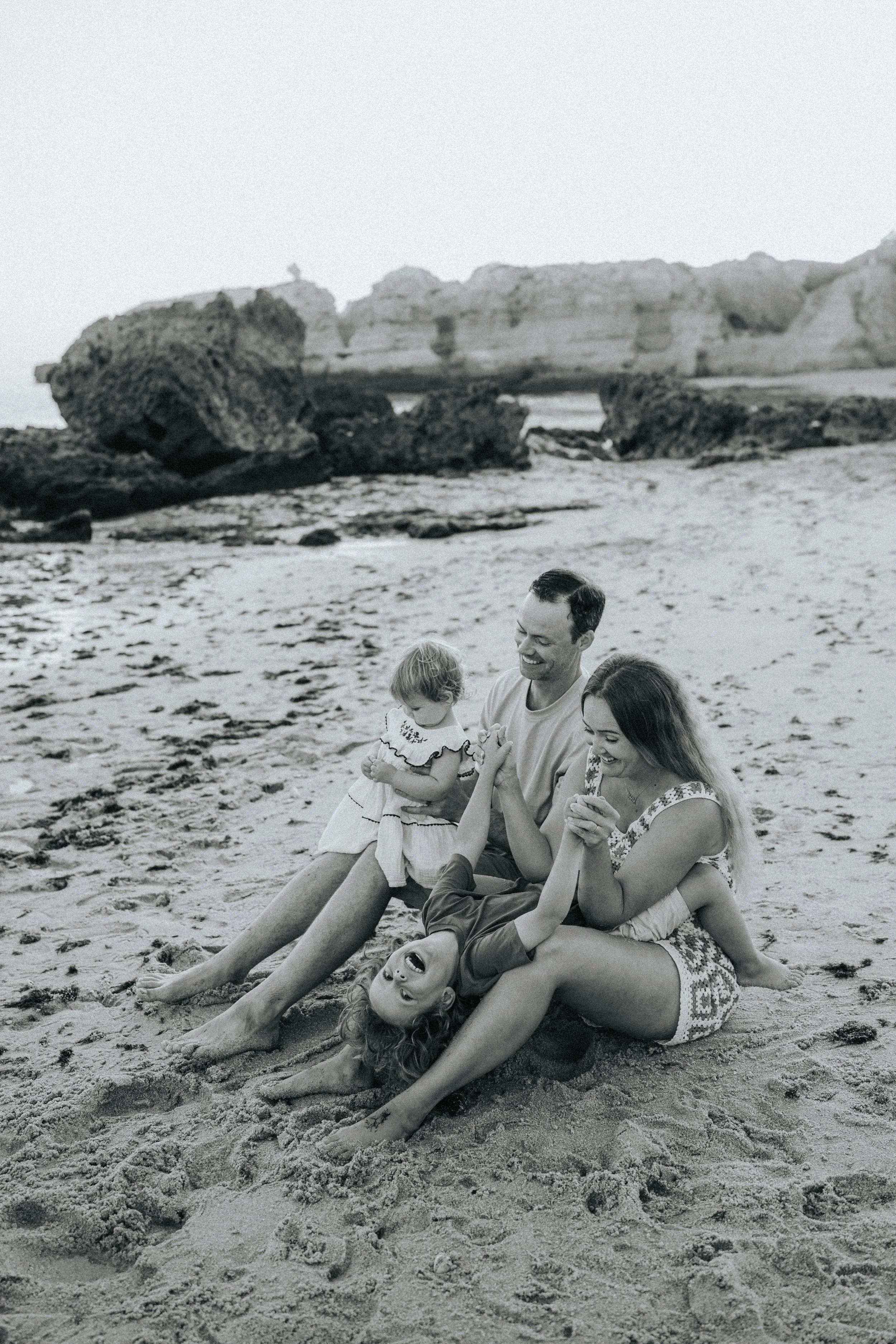 A family sitting and playing on the beach, with cliffs in the background, captured in black and white.