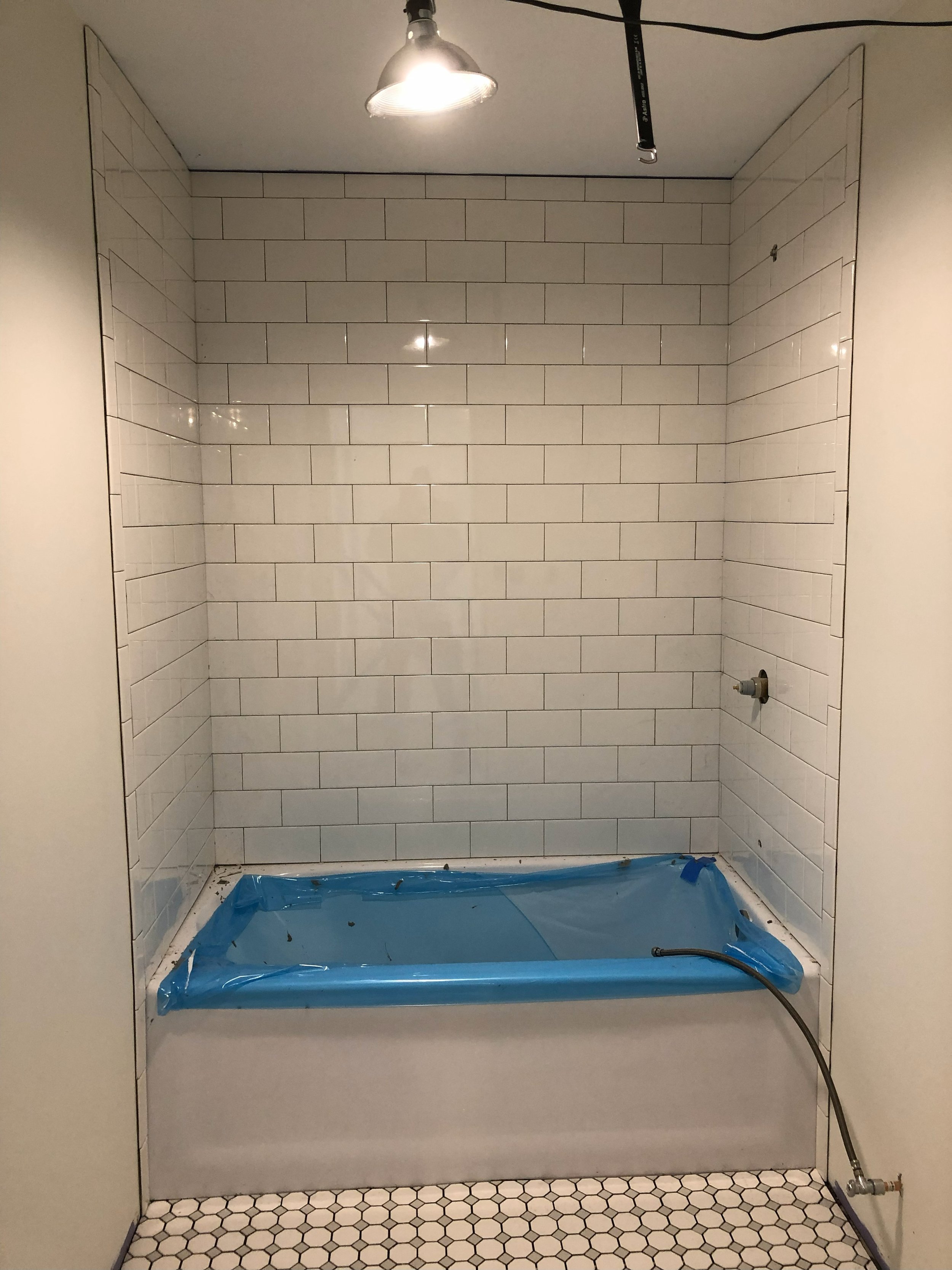 Bathroom shower area under renovation with white subway tile walls, a temporary blue plastic liner on the tub, and a ceiling light