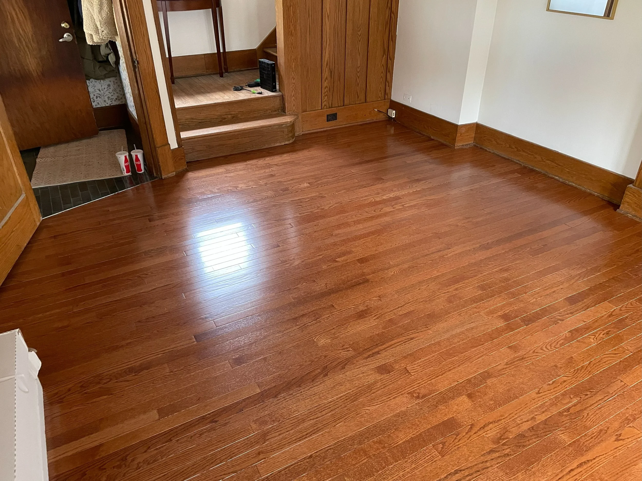 Empty room with polished hardwood floors, wooden trim, and stairs leading to an upper floor