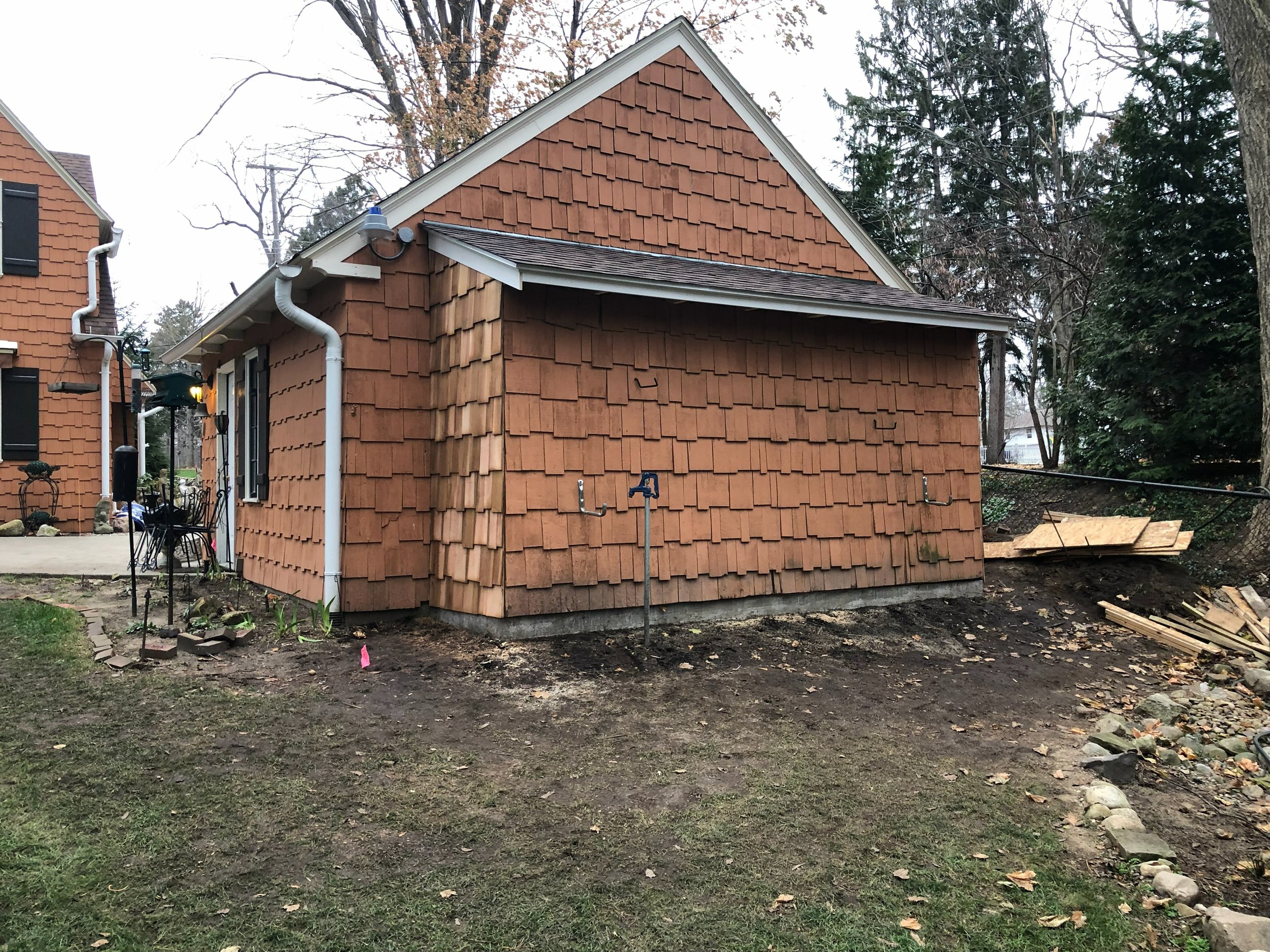 Backyard view of a house under construction with new shingles, empty ground, outdoor faucet, and scattered wood.