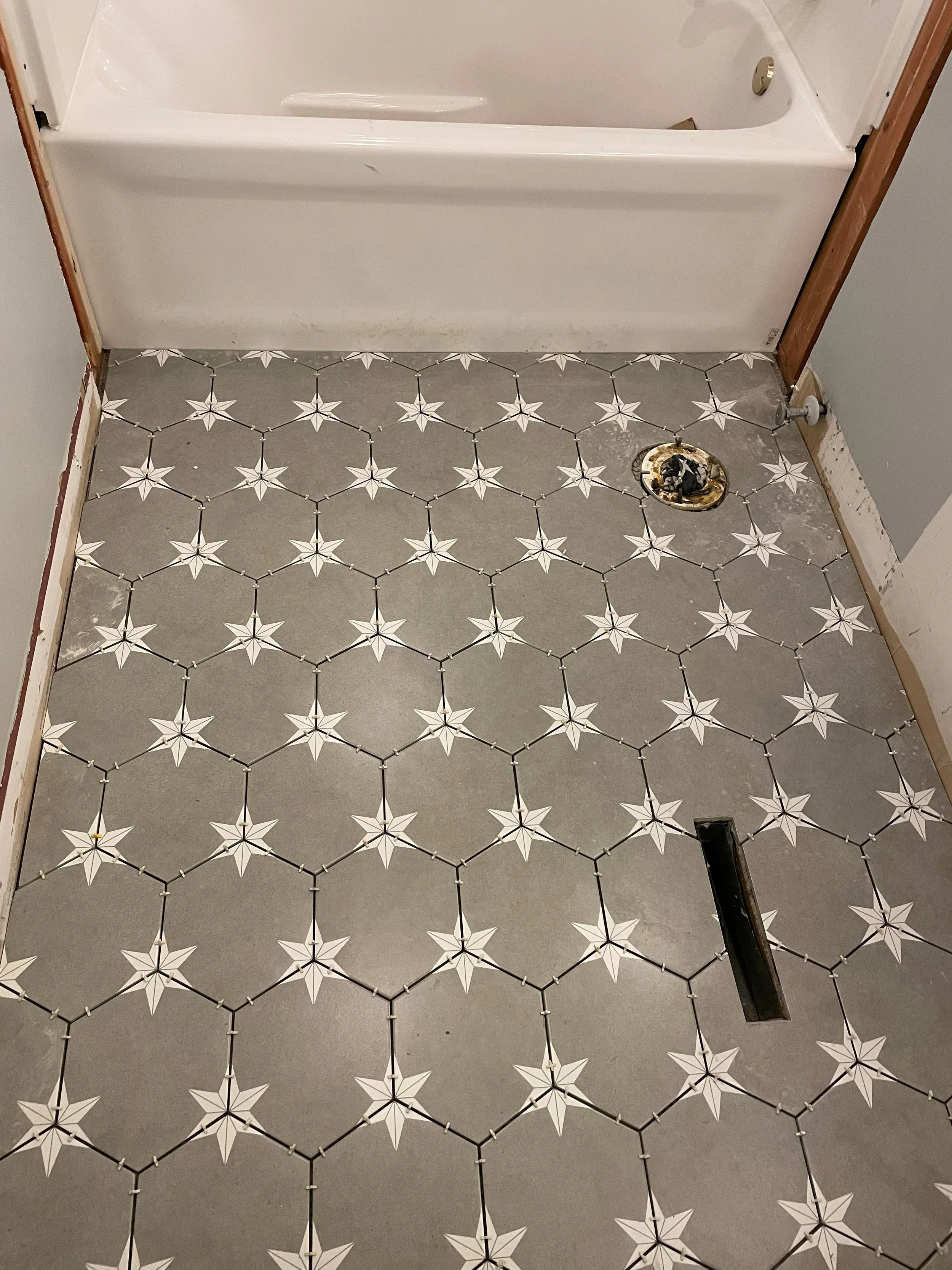 Bathroom floor with patterned tiles, partially removed for renovations, with plumbing exposed near the bathtub.