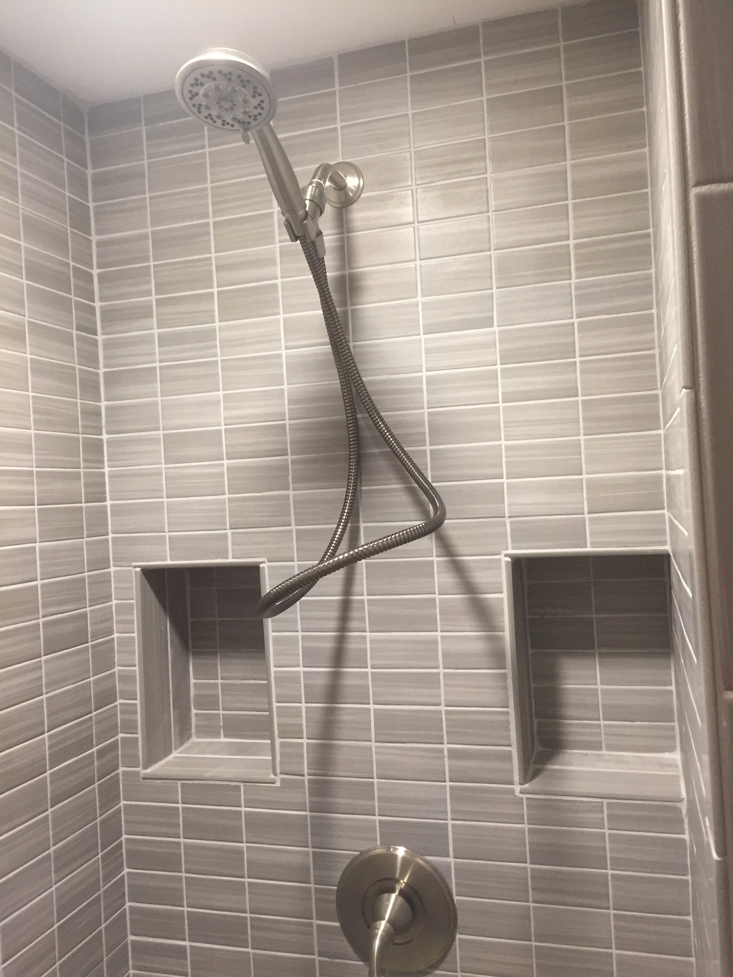 Showerhead with flexible hose and built-in recessed shelves in a tiled shower wall.