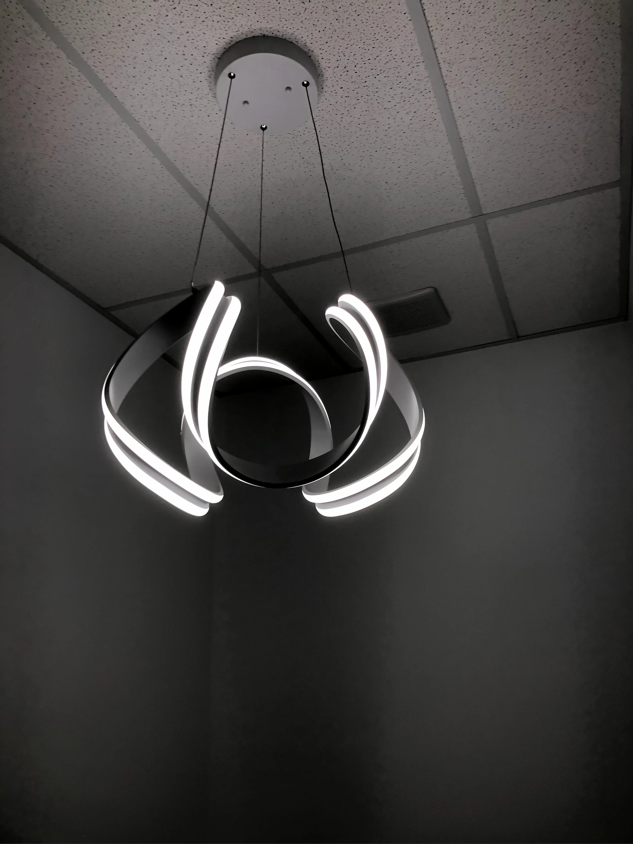 Modern ceiling light fixture with illuminated loops hanging from a white ceiling in a dimly lit room.