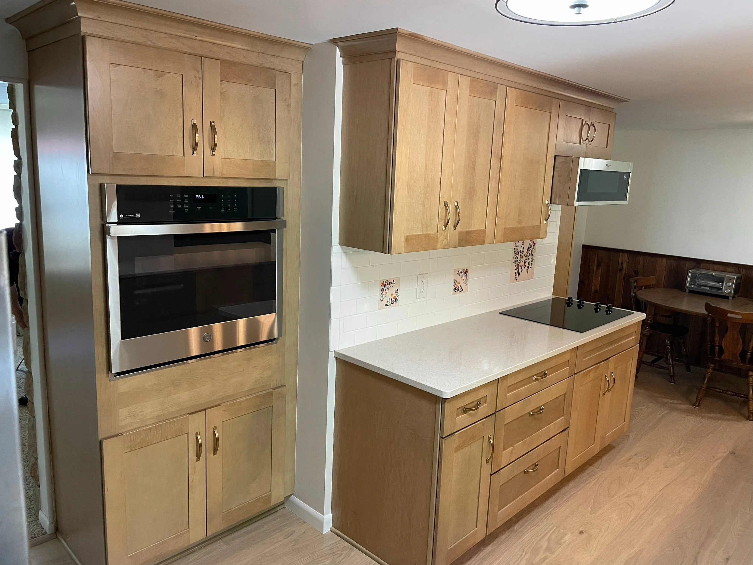 Kitchen with wooden cabinets, stainless steel oven, white countertop, and a black cooktop. There is a small table with chairs and an old-fashioned radio in the background.