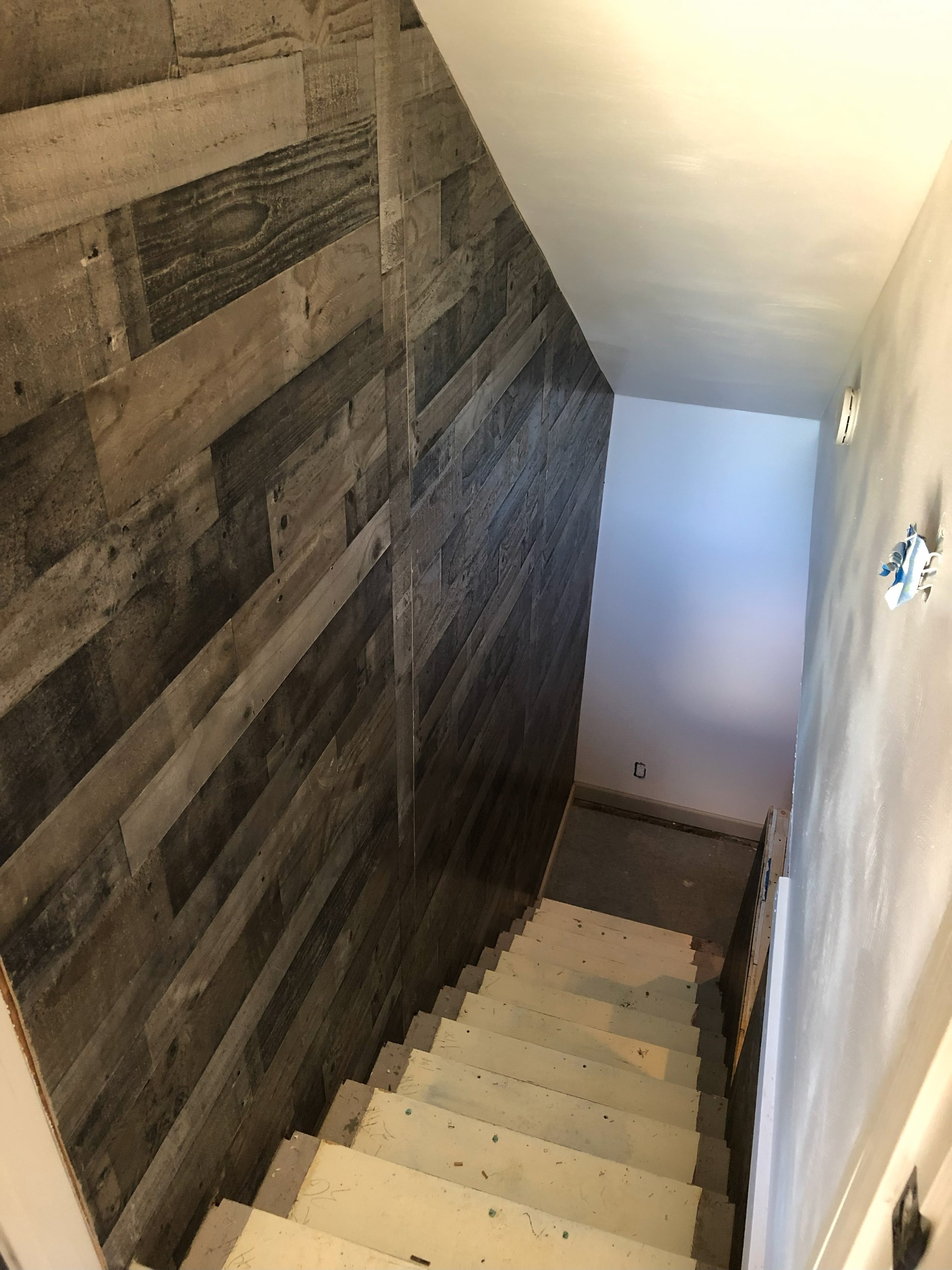 A staircase inside a house with a wooden wall on the left and a plain white wall on the right. The stairs are still under construction.