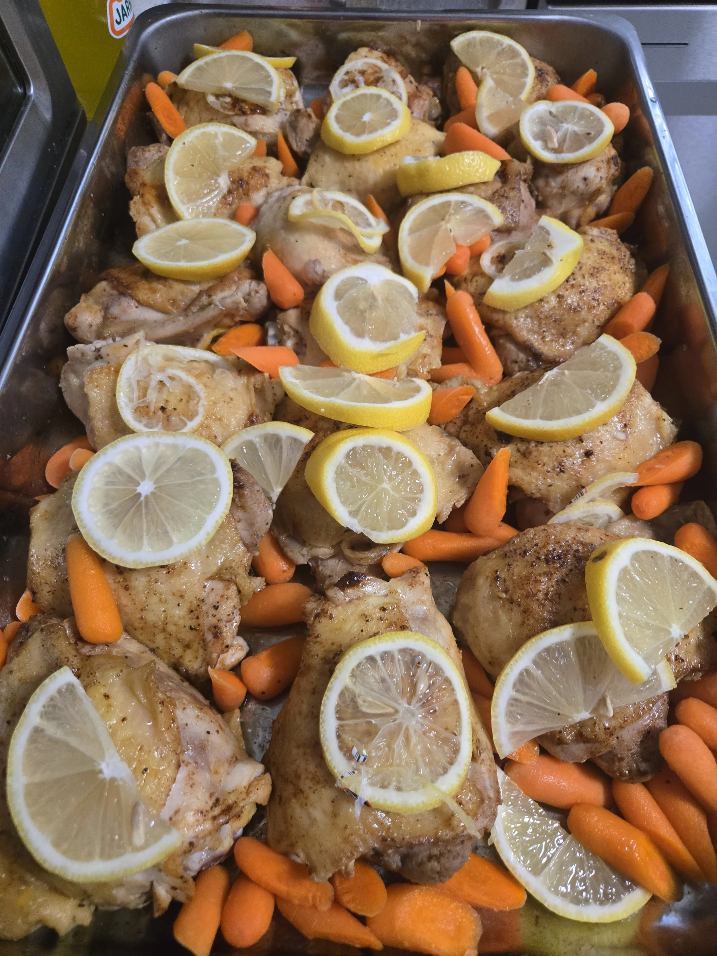 Lemon-herb roasted chicken with tender cooked carrots served in a stainless steel buffet pan by Acento ATX