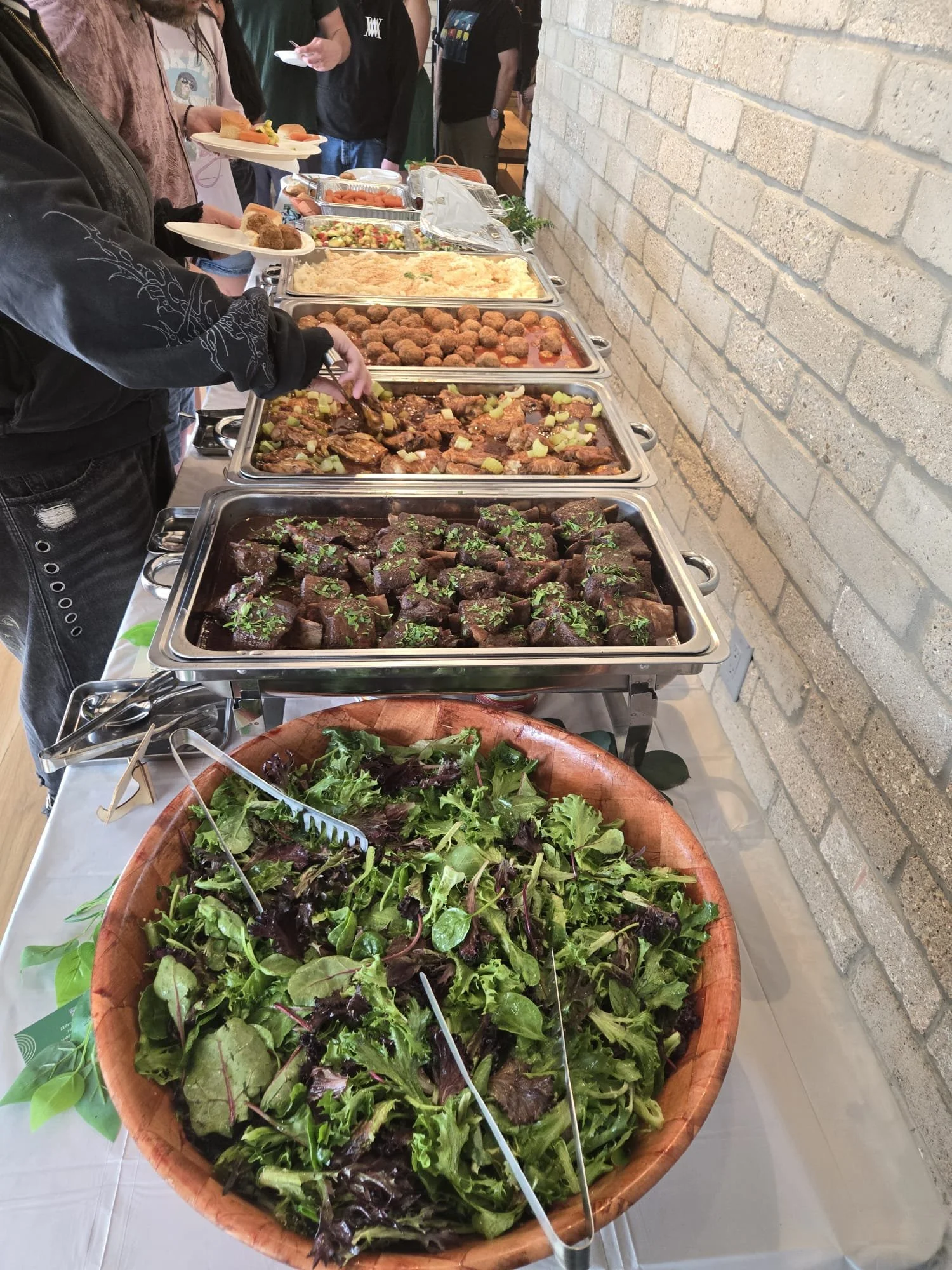 Interactive buffet station featuring leafy salads, braised meats, and fried bites for group dining by Acento ATX