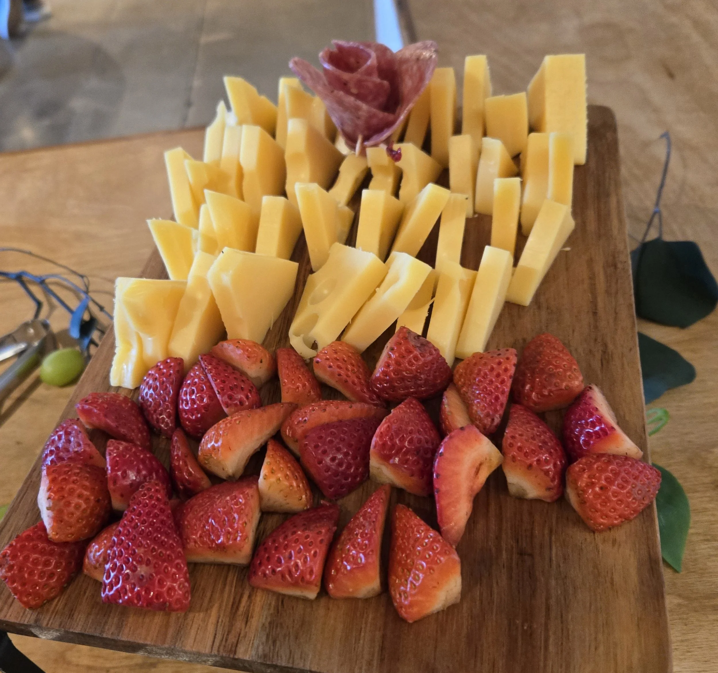 Wooden charcuterie tray with sliced yellow cheese, fresh strawberries, and cured salami by Acento catering in Austin TX