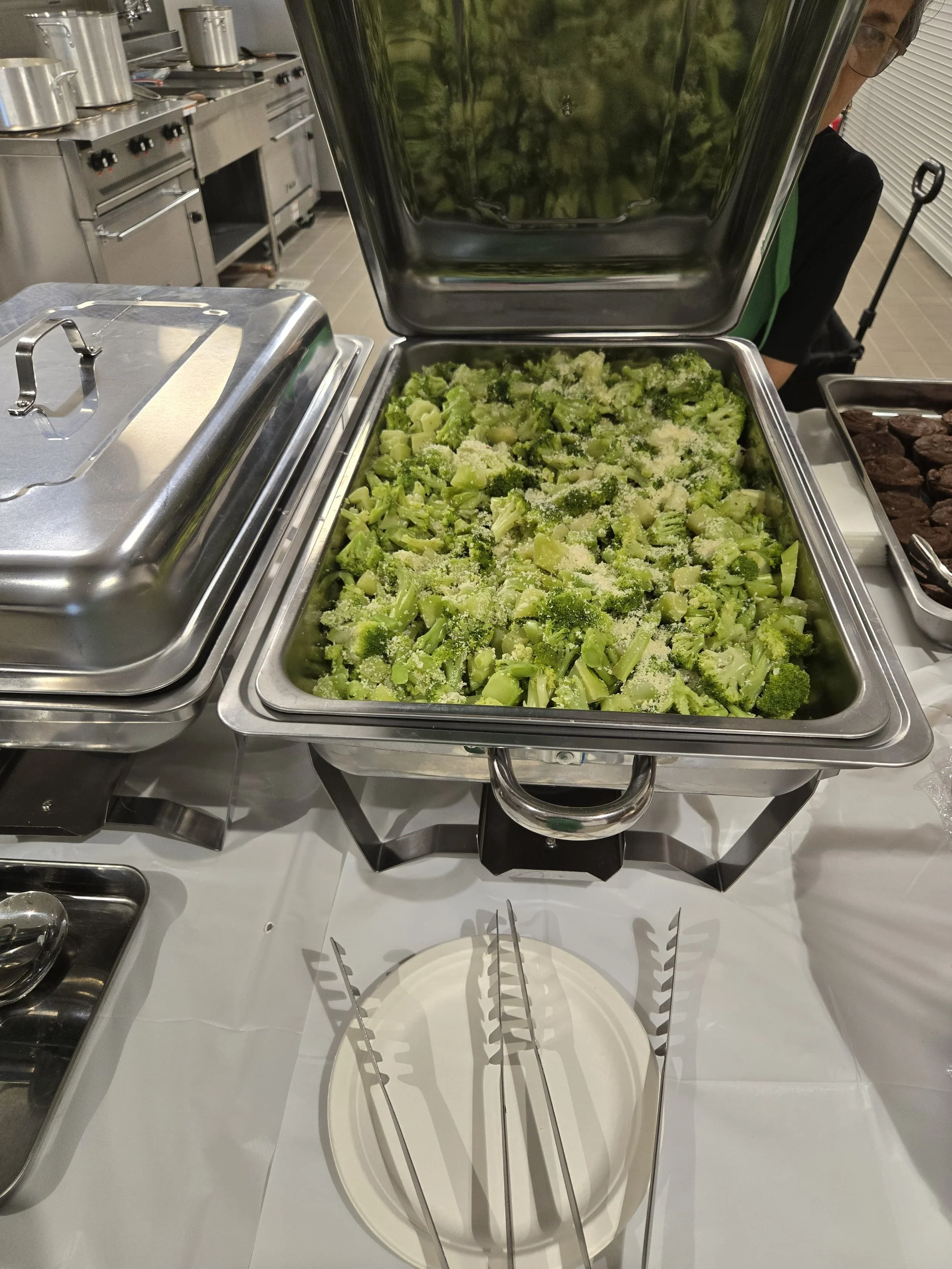 Stainless steel chafing dish filled with steamed broccoli topped with seasoned cheese by Acento catering in Austin TX