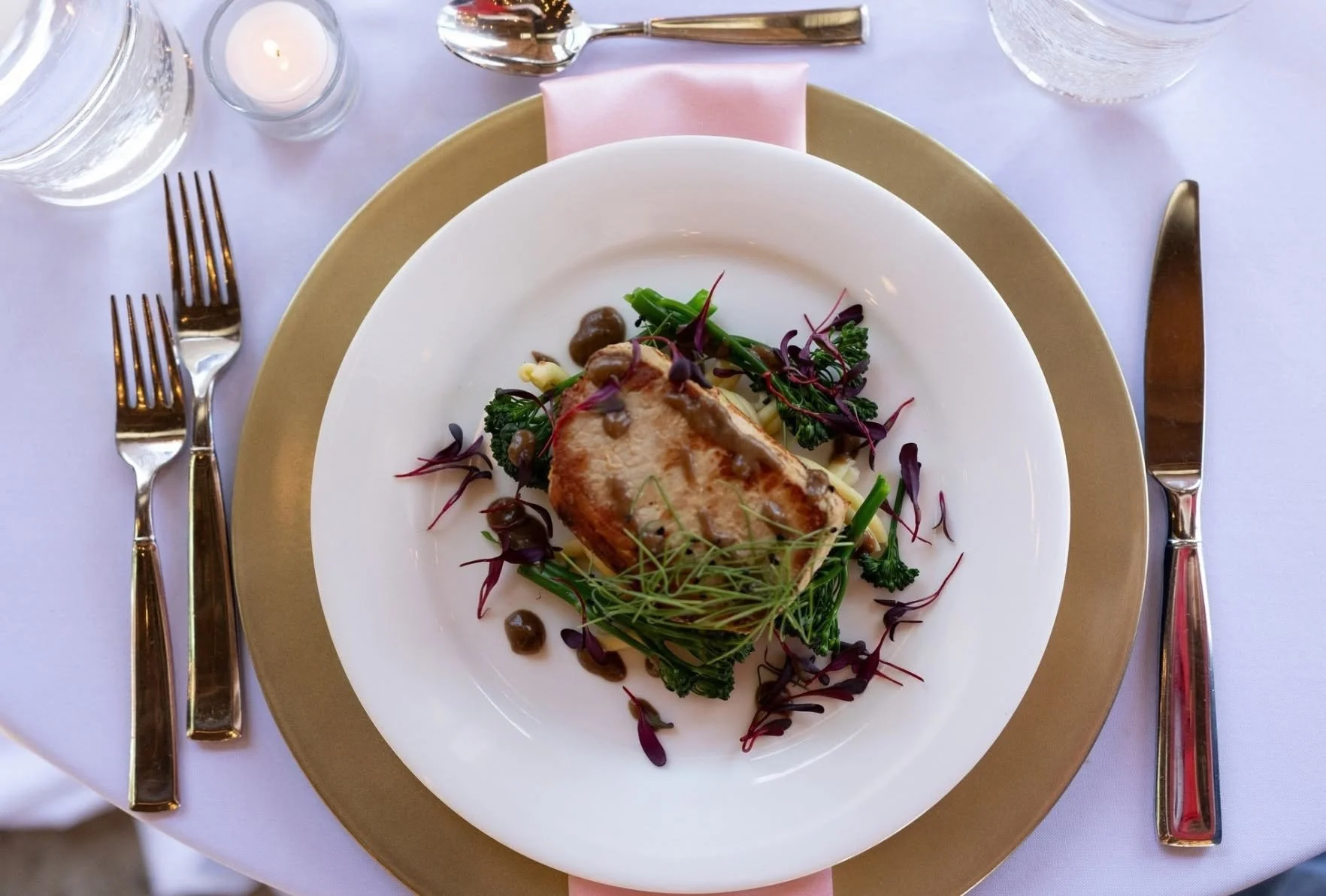Plated entrée by City Catering in Knoxville featuring a seared pork chop with broccolini, microgreens, and sauce on an elegant place setting.